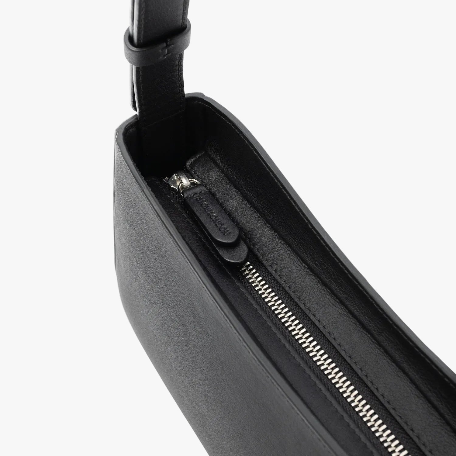 Close up of the zip closure and STOW London embossed pull tabs on Stow London's Post Shoulder in Black smooth leather on a light grey background featuring silver stainless steel hardware