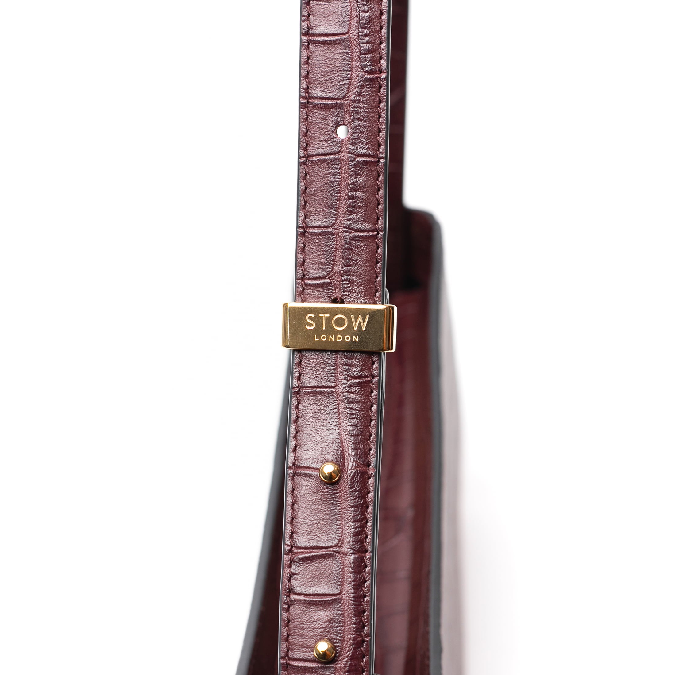 Close up of strap, gold-coated stainless steel hardware and brand engraving on STOW London's Post Shoulder bag in Burgundy Embossed Croc leather on a white background
