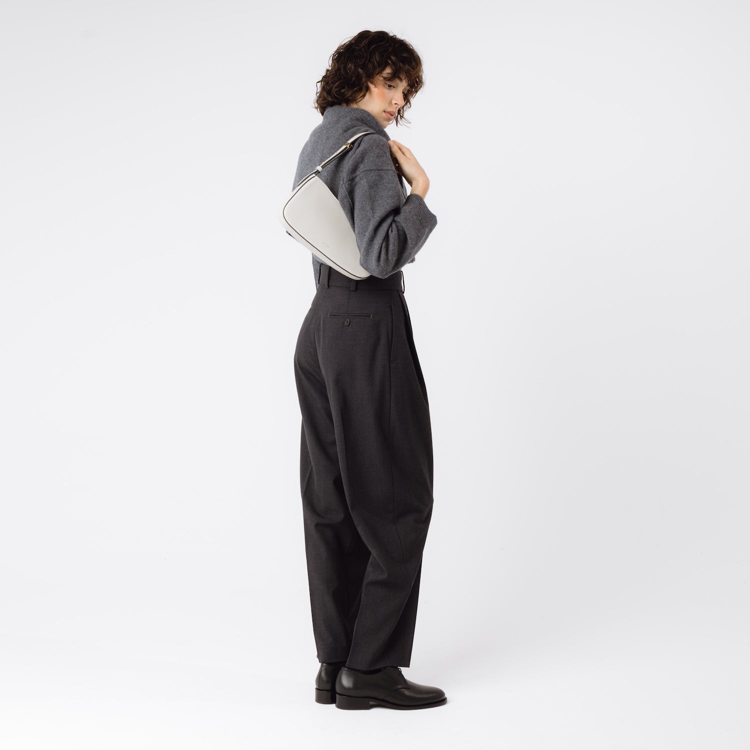 Model wearing STOW London's Post Shoulder bag in Cloud Grey smooth leather on her shoulder featuring gold-coated stainless steel hardware on a white background