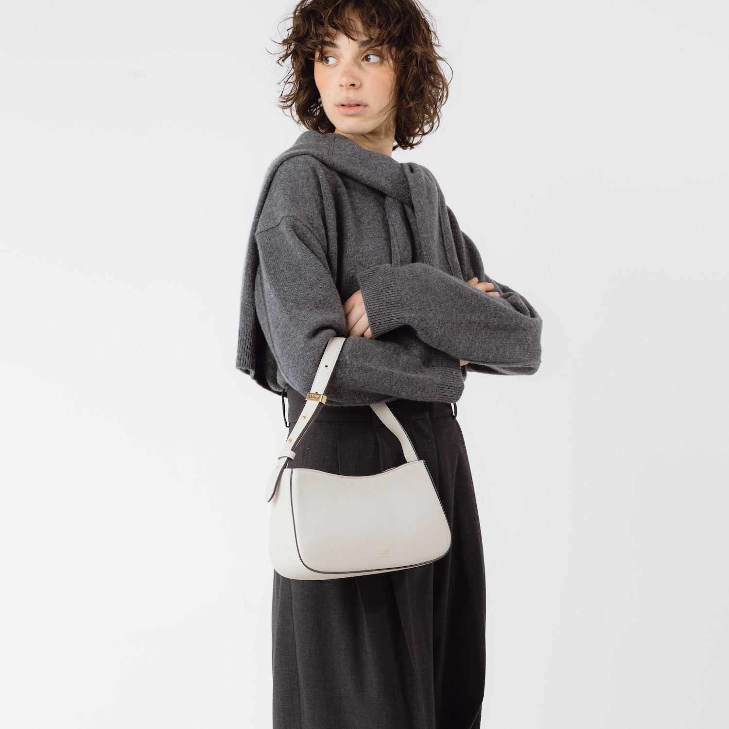 Model wearing STOW London's Post Shoulder bag in Cloud Grey smooth leather on her arm featuring gold-coated stainless steel hardware on a white background