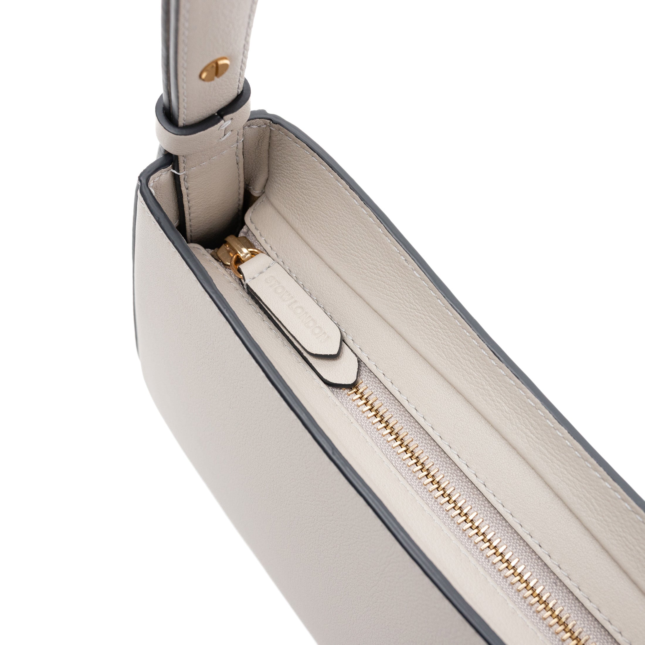 Close up of zip top closure of STOW London's Post Shoulder bag in Cloud Grey smooth leather featuring gold-coated stainless steel hardware and brand engraving on pull tab on a white background