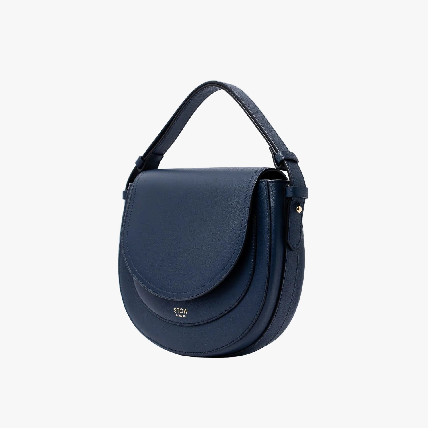 Off-axis view of STOW London's Saddle bag in Navy smooth leather and its short top handle on a light grey background