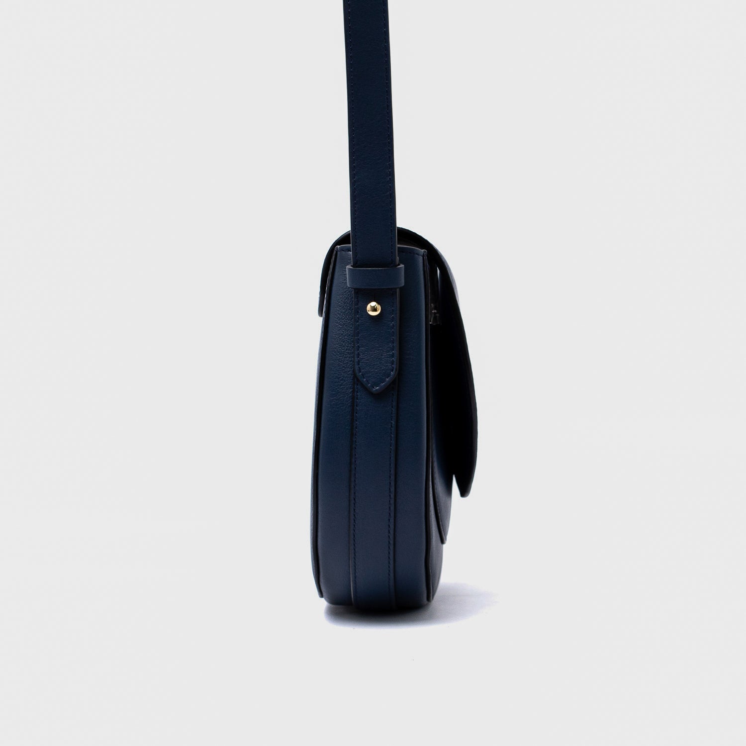 Side view of STOW London's Saddle bag in Navy smooth leather on a light grey background