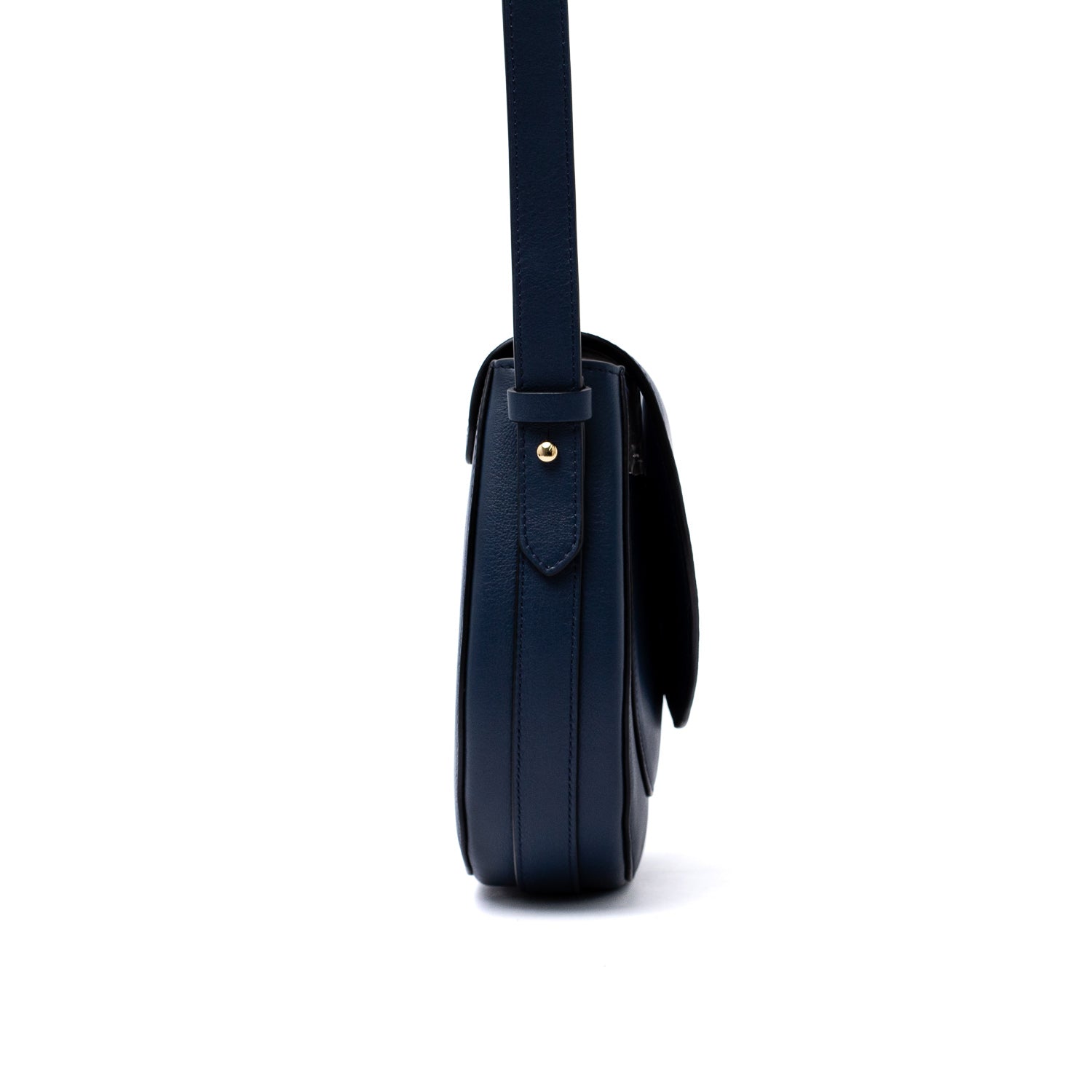 Side view of STOW London's Saddle bag in Navy smooth leather featuring gold-coated stainless steel hardware and the detachable crossbody strap on a white background