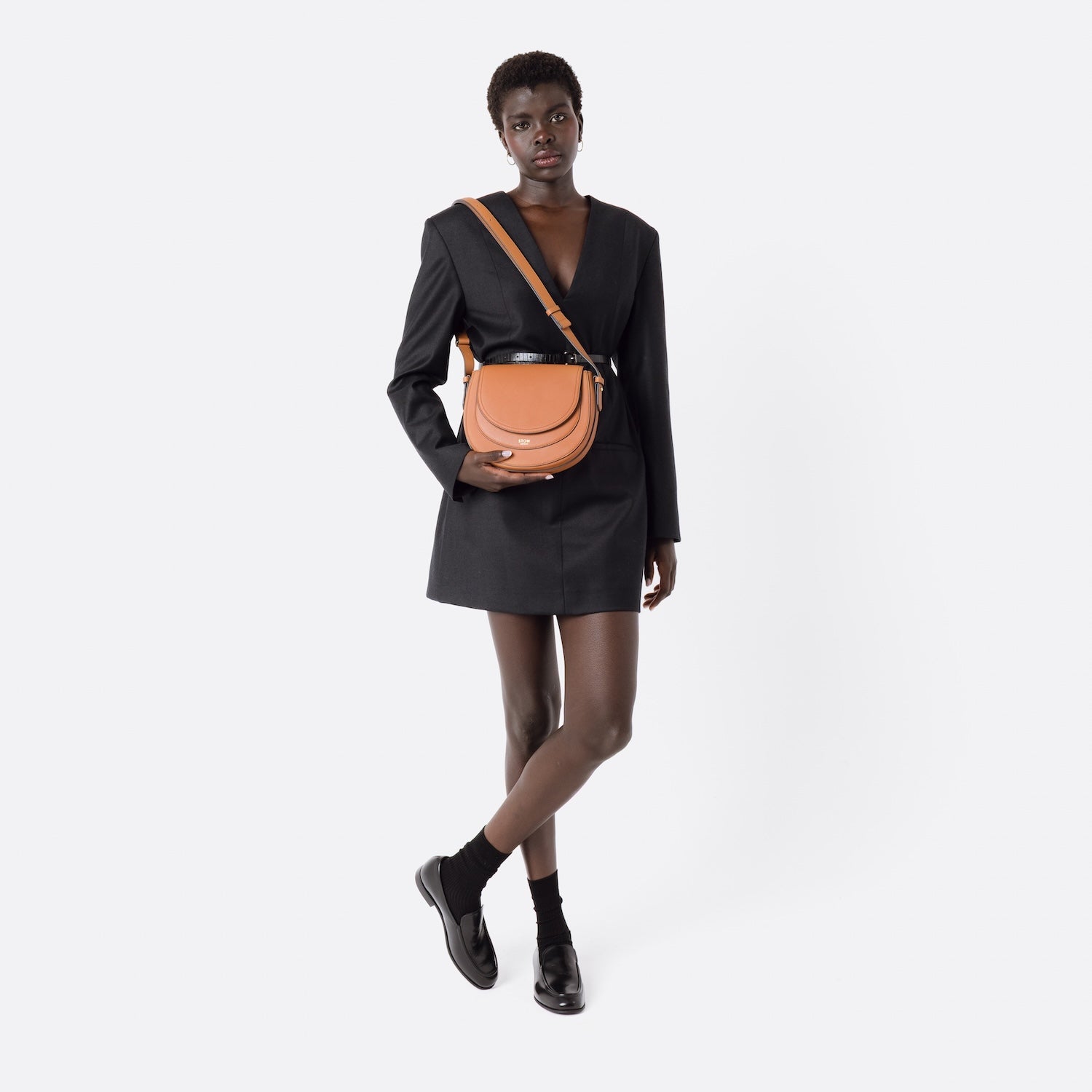Model wearing STOW London's Saddle bag in Earth Tan smooth leather on her shoulder with detachable strap on a white background