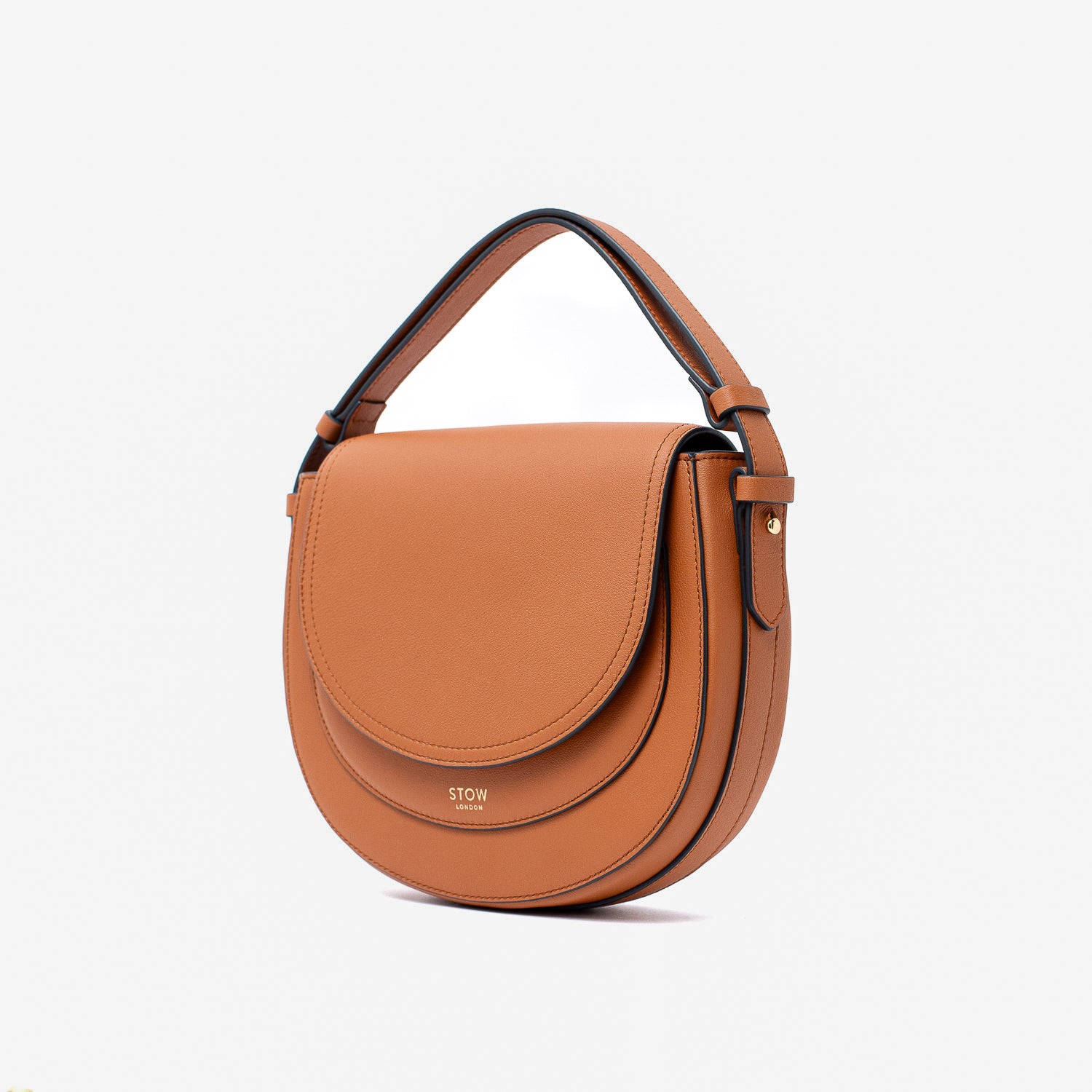Off-axis view of STOW London's Saddle bag in Earth Tan smooth leather with its short top handle on a light grey background