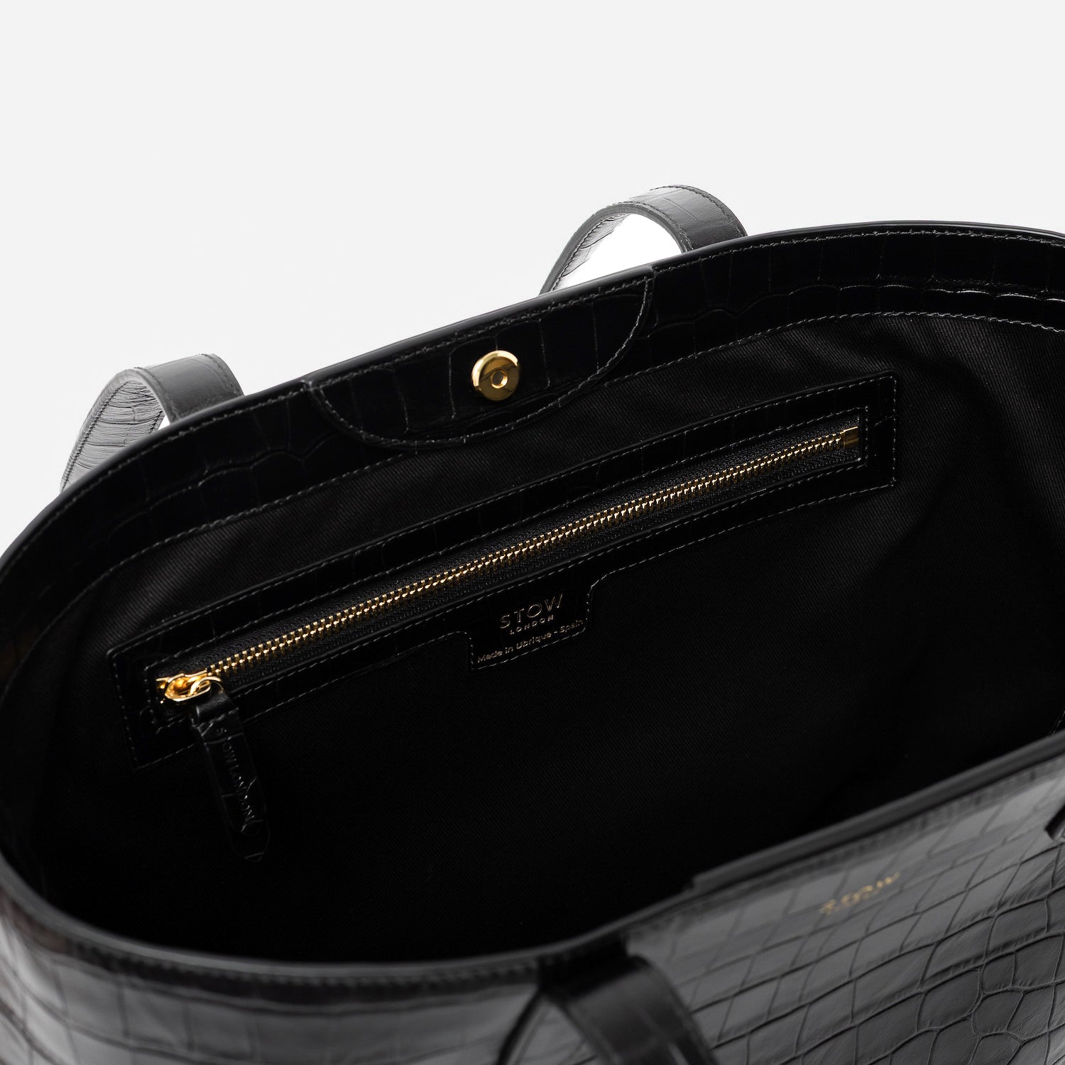 Close up of Stow London's Everyday Tote Bag in Black Embossed Croc leather on a light grey background featuring zip pocket, magnetic closure and gold hardware