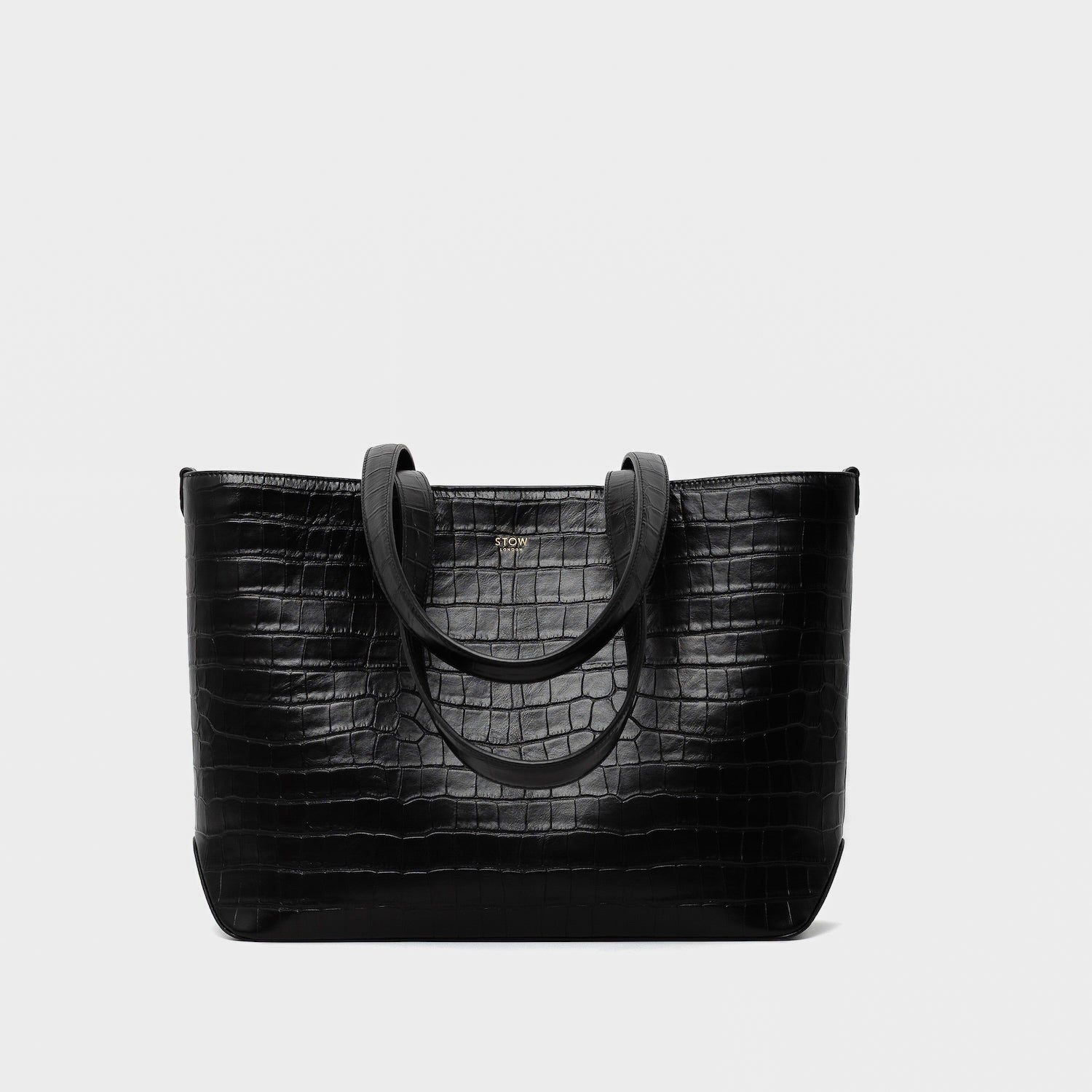 Stow London's Everyday Tote Bag in Black Embossed Croc leather on a light grey background featuring gold STOW logo