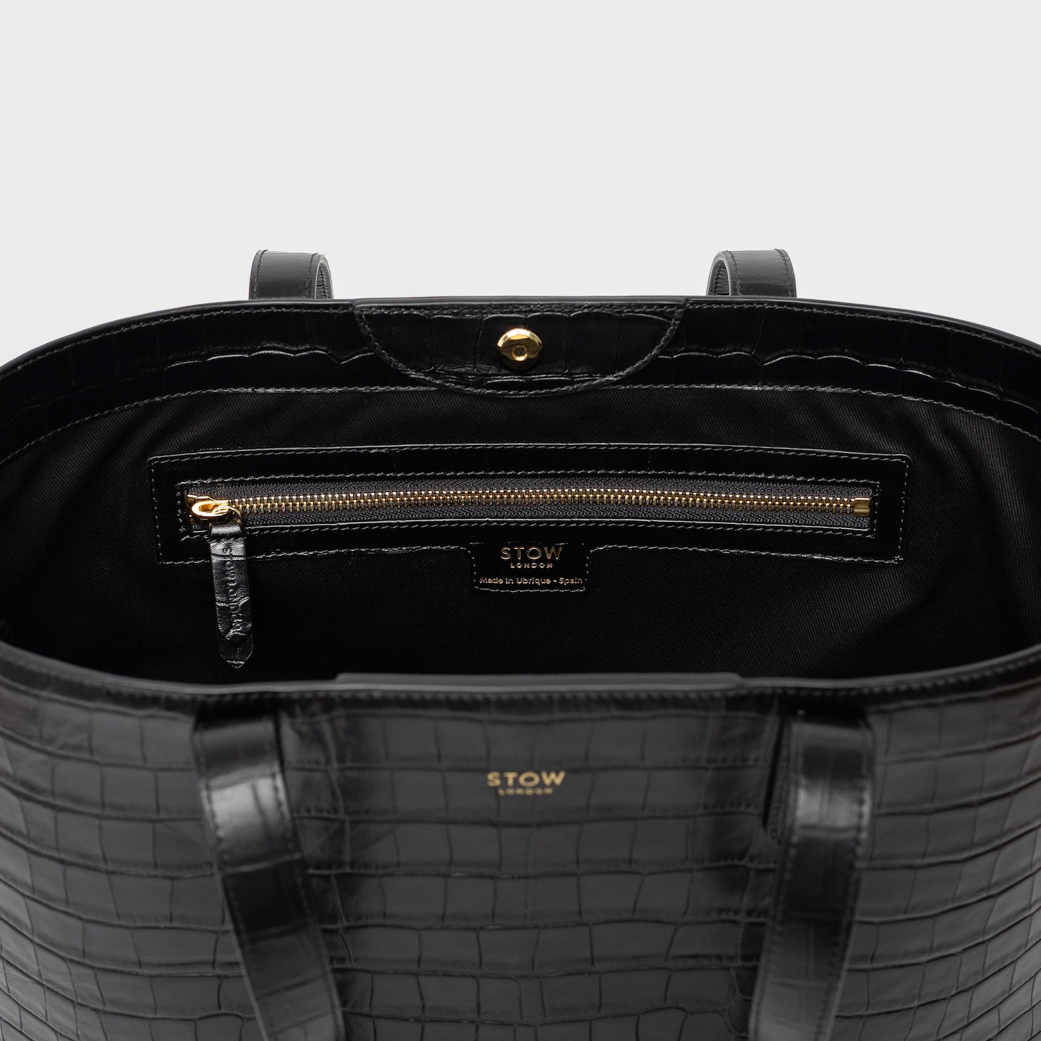 Close up of Stow London's Everyday Tote Bag in Black Embossed Croc leather on a light grey background featuring zip pocket, magnetic closure and gold hardware