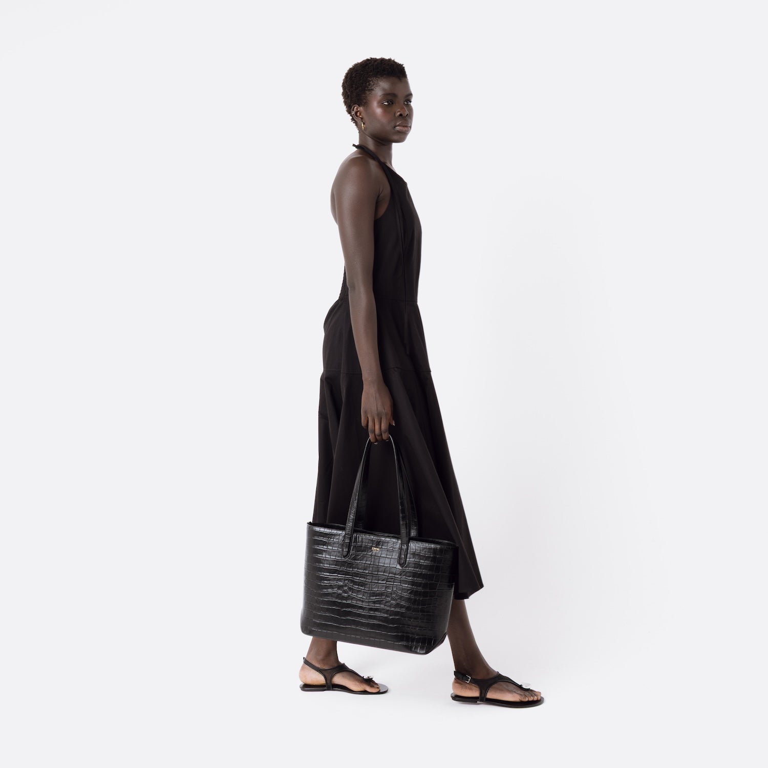 Model holding Stow London's Everyday Tote Bag in Black Embossed Croc leather at her side on a white background