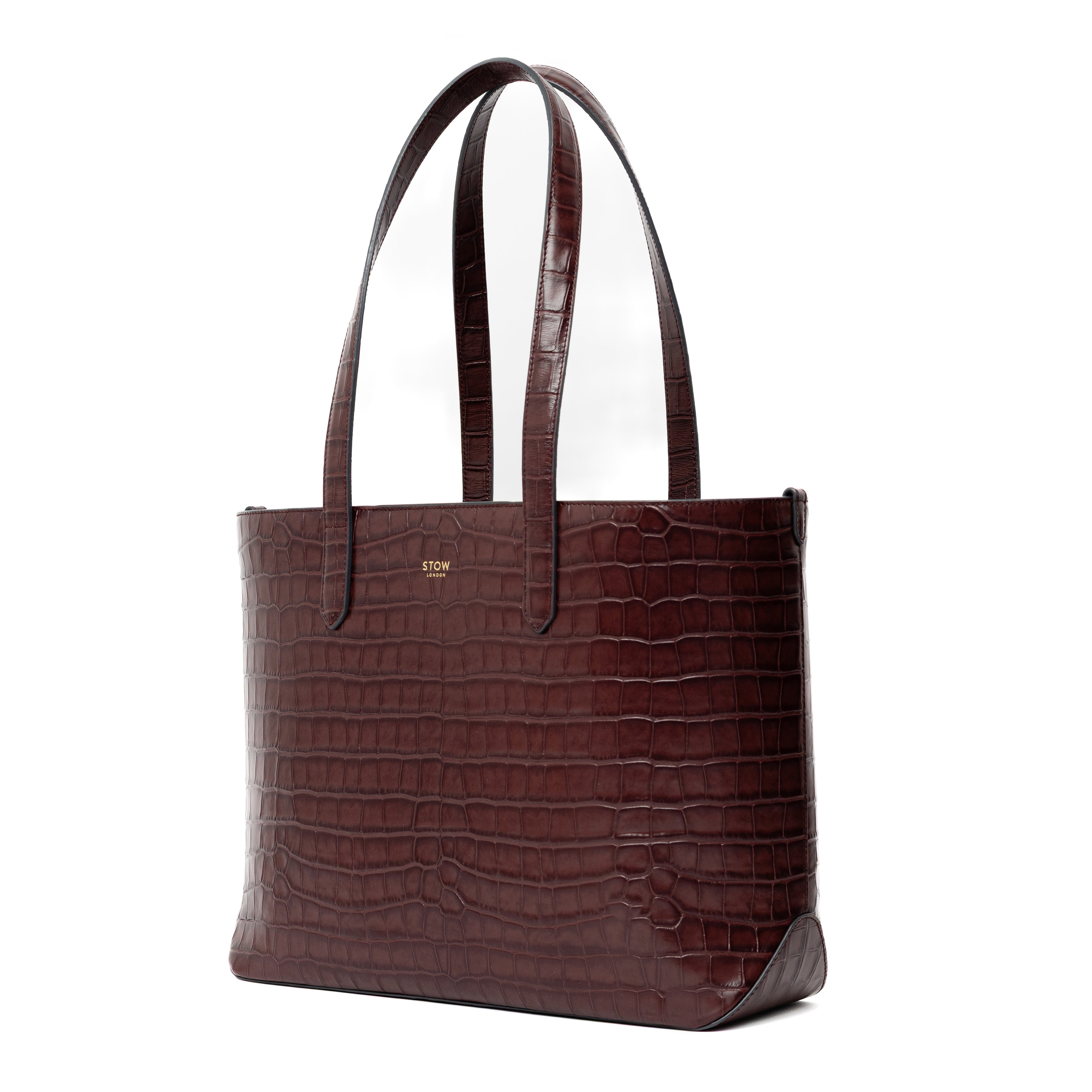 Off-axis view of Stow London's Everyday Tote Bag in Burgundy Embossed Croc leather shown on a white background with gold Stow logo