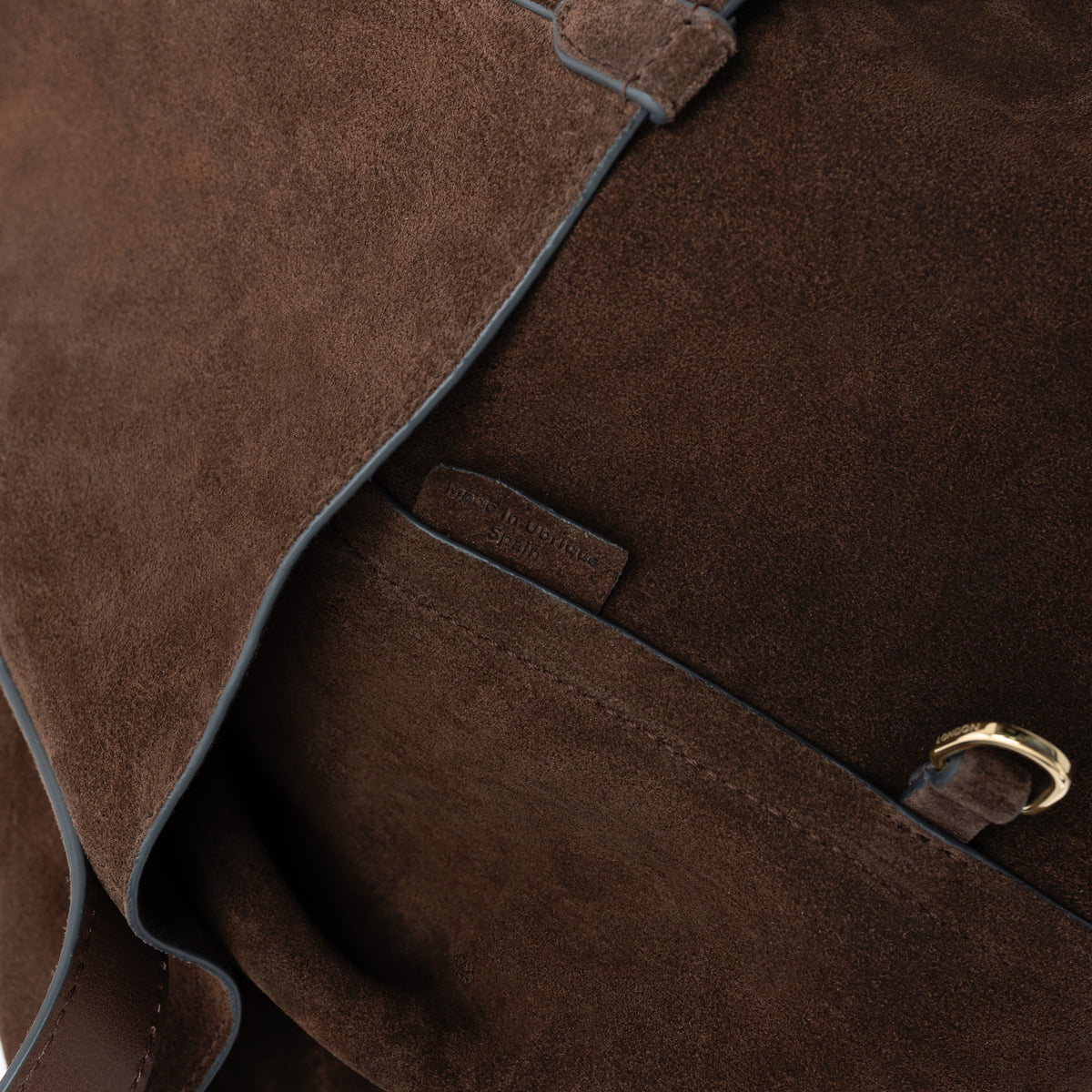 Close up of the suede interior of STOW London's Everyday Tote bag in Chocolate on a light grey background featuring a small d-ring and Made in Ubrique tag