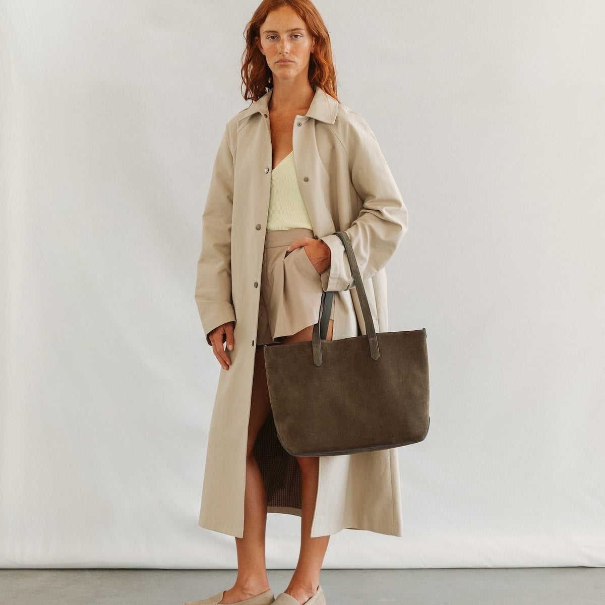 Model wearing STOW London's Everyday Tote bag in Dark Green suede featuring a small STOW London logo embossed on the front panel