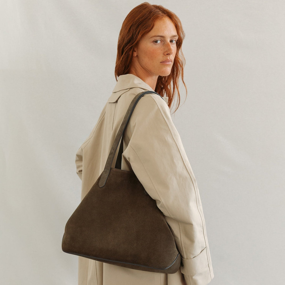 Model wearing STOW London's Everyday Tote bag in Dark Green suede on a light grey background featuring a small STOW London logo embossed on the front panel