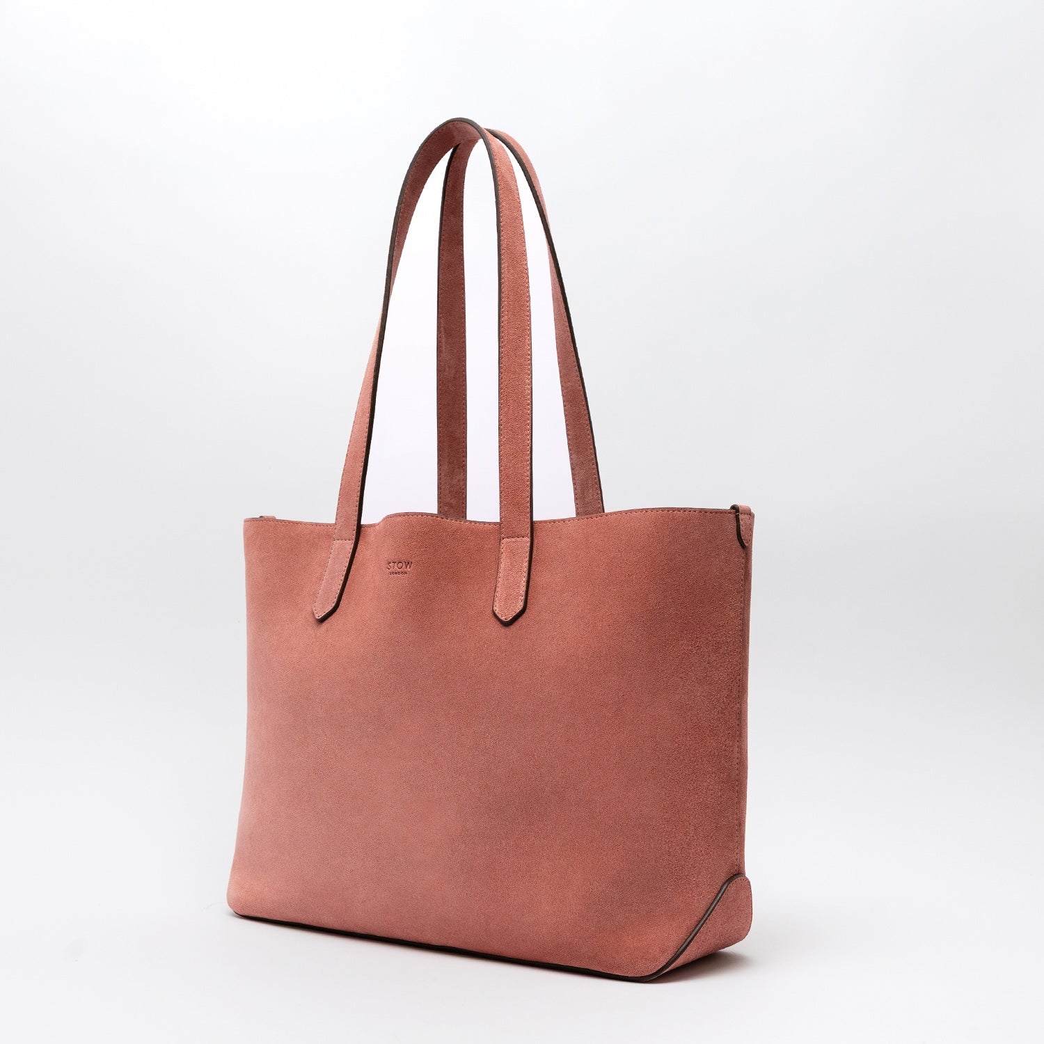 Off-axis view of STOW London's Everyday Tote bag in Hazy Blush suede on a light grey background featuring a small STOW London logo embossed on the front panel