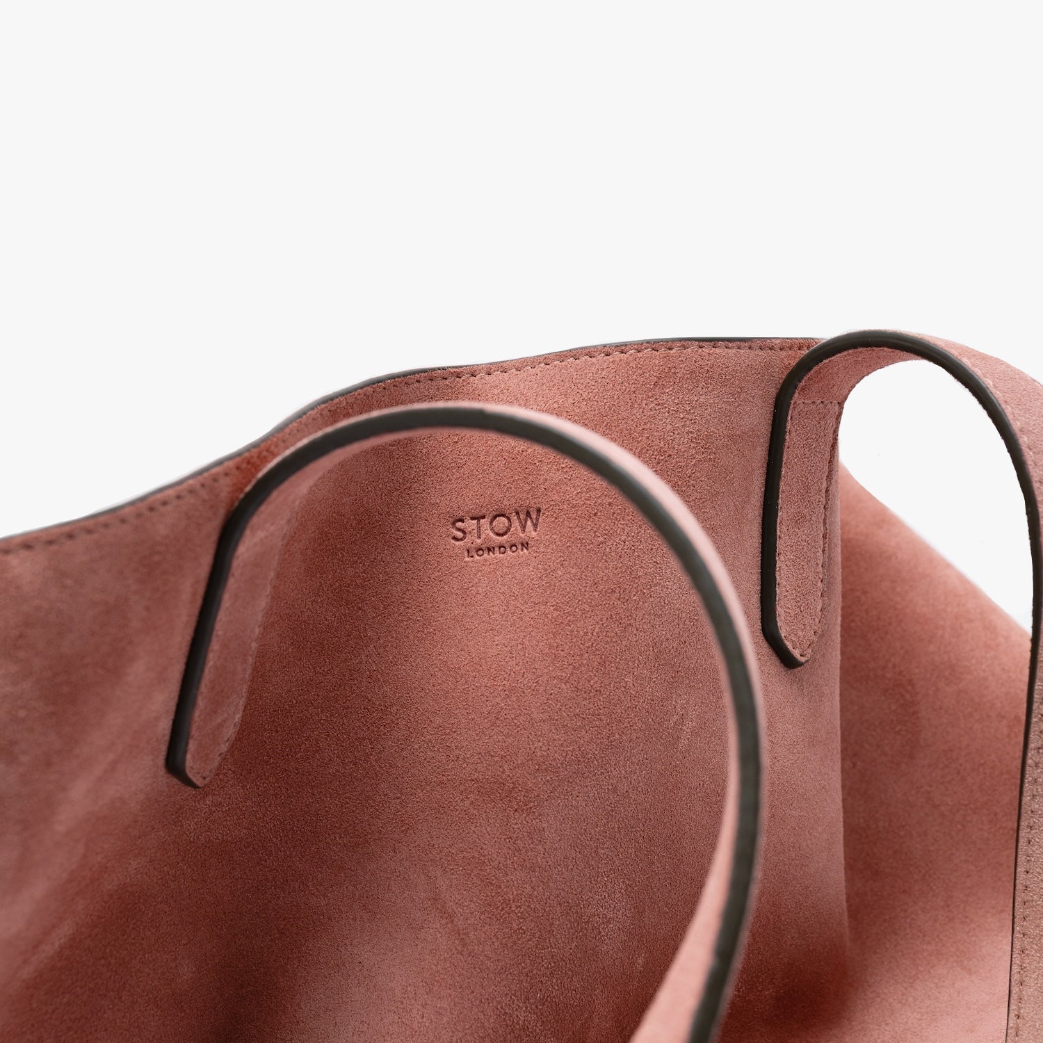 Close up of STOW London's Everyday Tote bag in Hazy Blush suede on a light grey background featuring a small STOW London logo embossed on the front panel