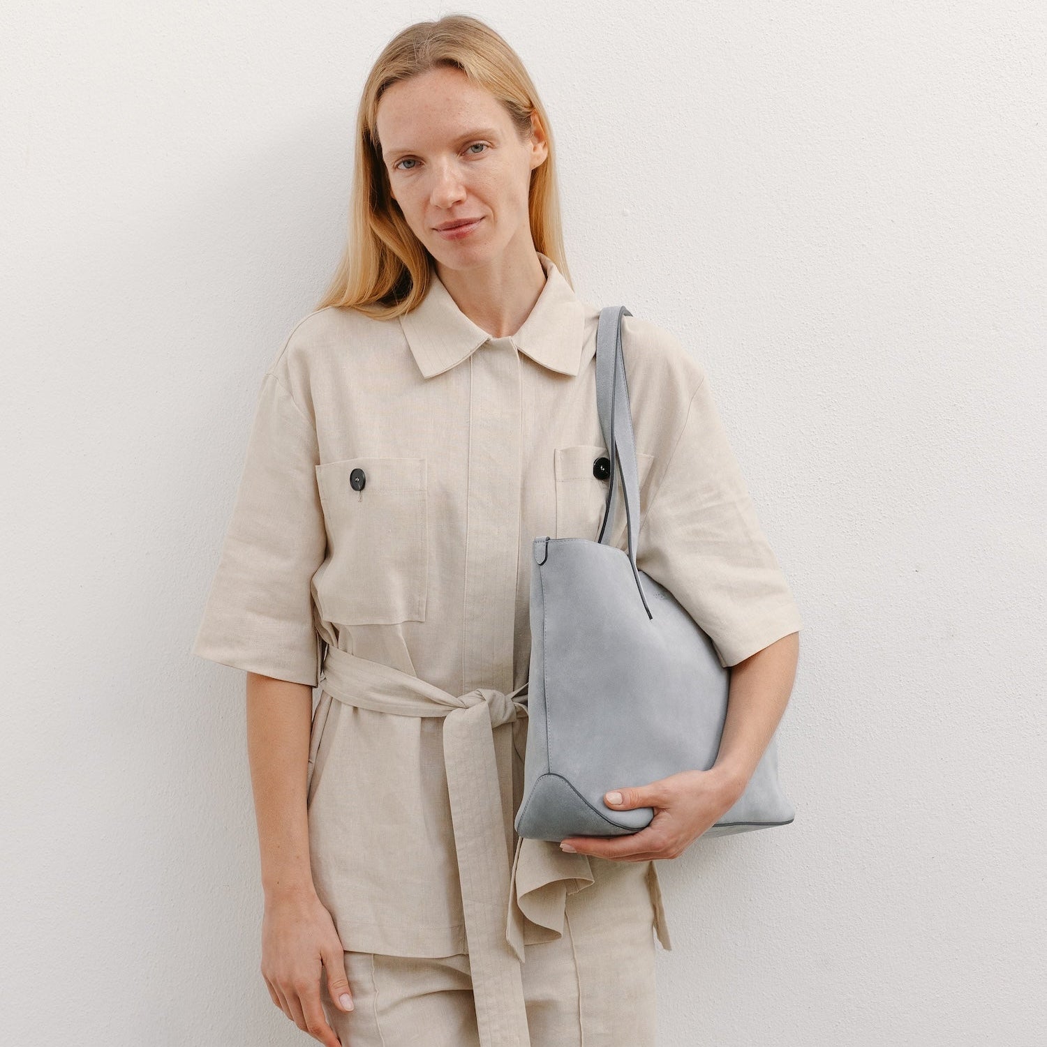 Model wearing STOW London's Everyday Tote bag in Misty Blue suede featuring a small STOW London logo embossed on the front panel