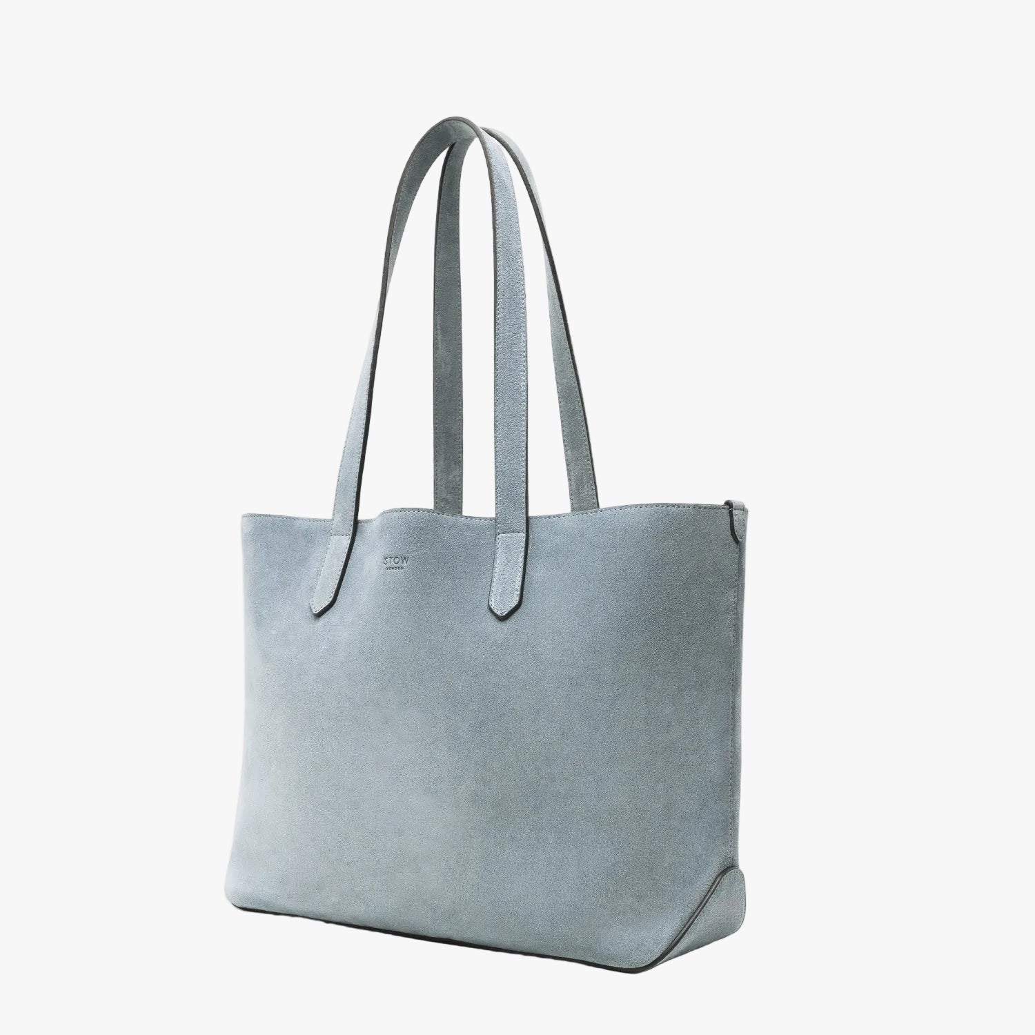 Off-axis view of STOW London's Everyday Tote bag in Misty Blue suede on a light grey background featuring a small STOW London logo embossed on the front panel