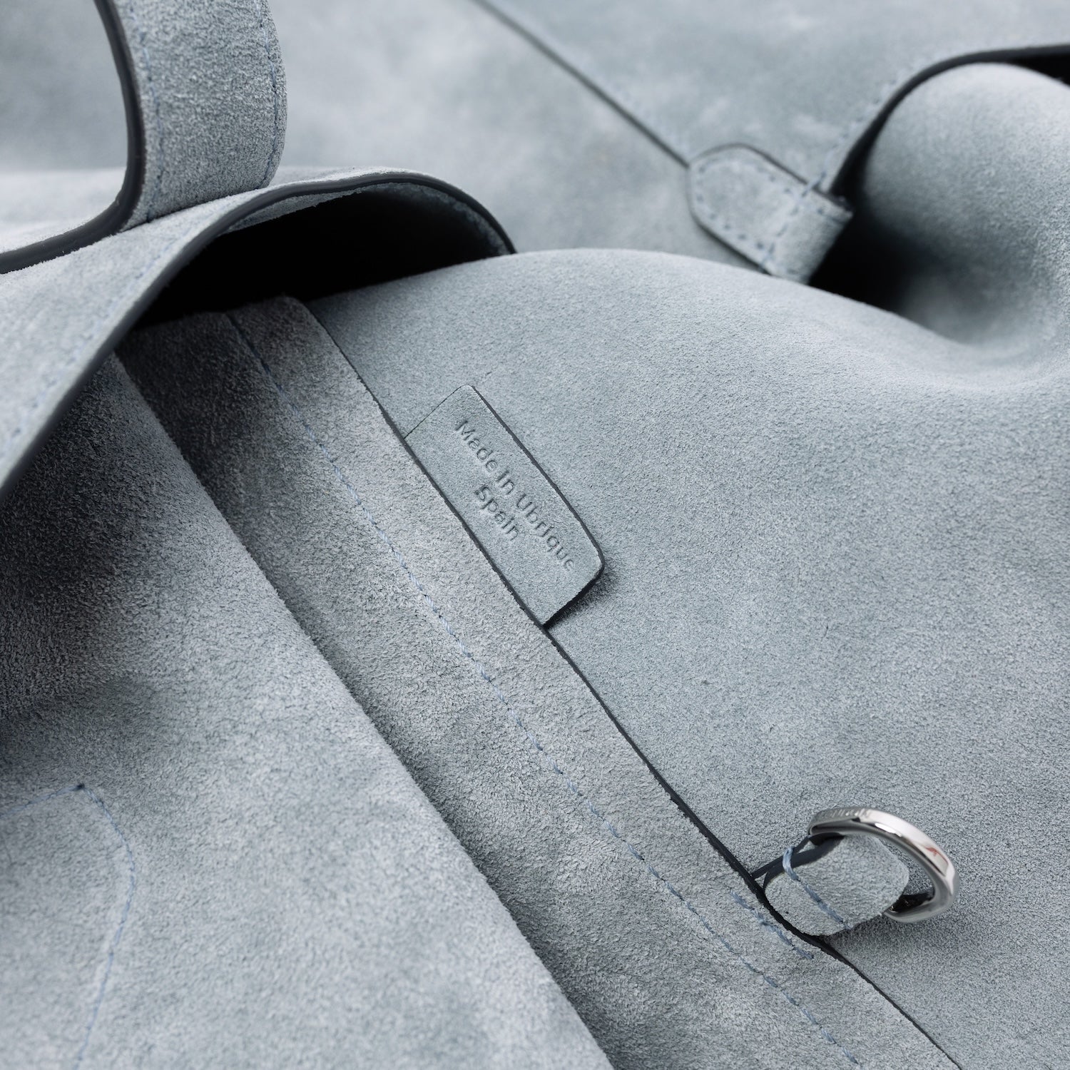Close up of the suede interior of STOW London's Everyday Tote bag in Misty Blue suede on a light grey background featuring the silver d-ring and Made in Ubrique tag
