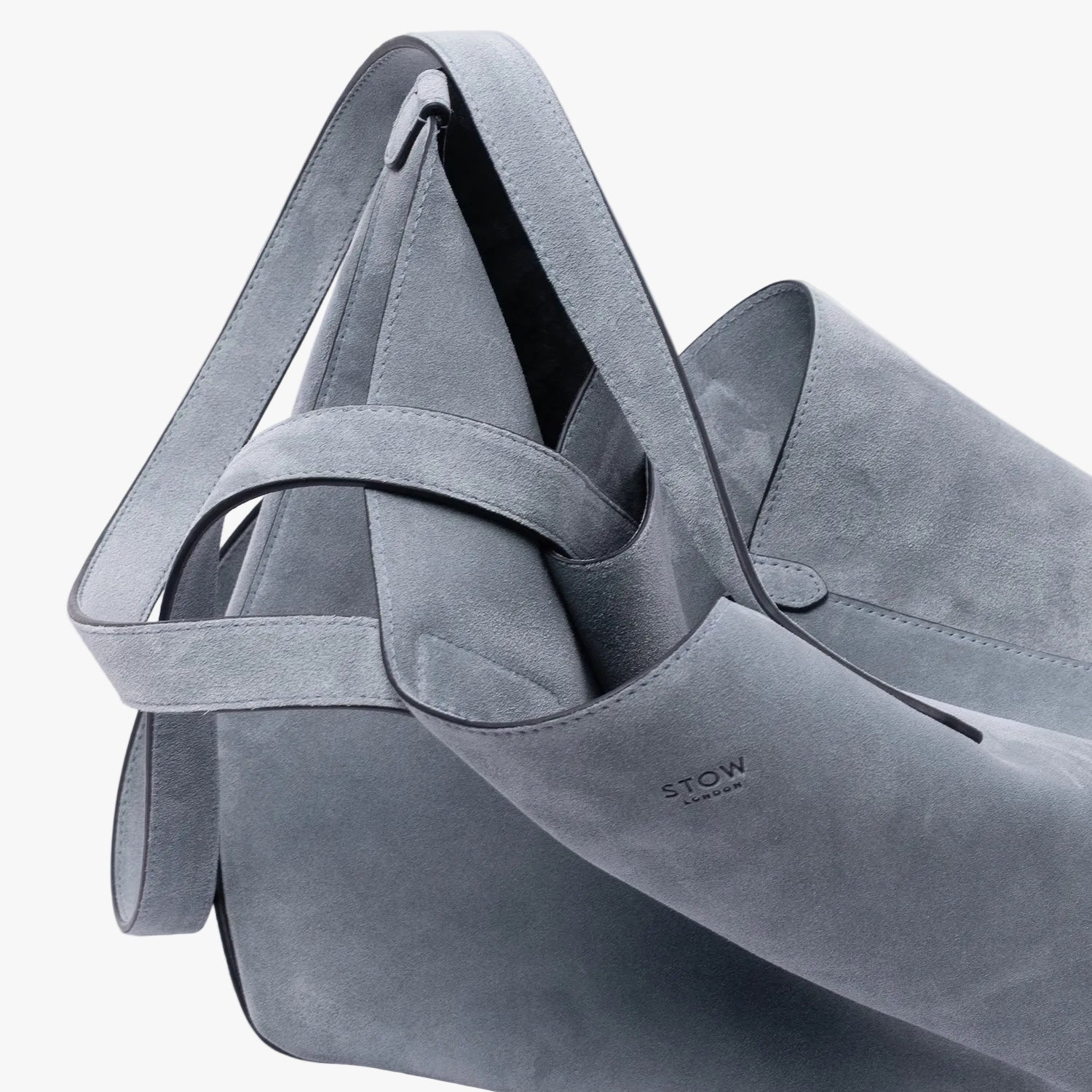Close up of STOW London's Everyday Tote bag in Misty Blue suede on a light grey background featuring a small STOW London logo embossed on the front panel