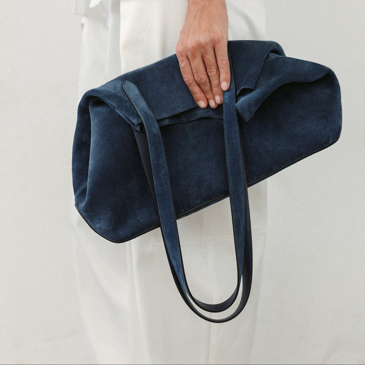 Model wearing white trousers holding STOW London's Everyday Tote bag in Navy suede