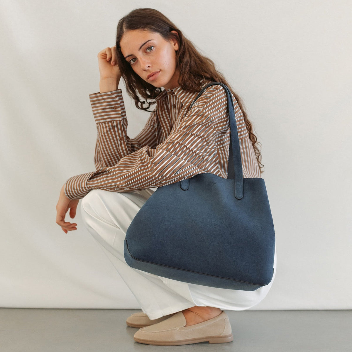 Model wearing STOW London's Everyday Tote bag in Navy suede featuring a small STOW London logo embossed on the front panel