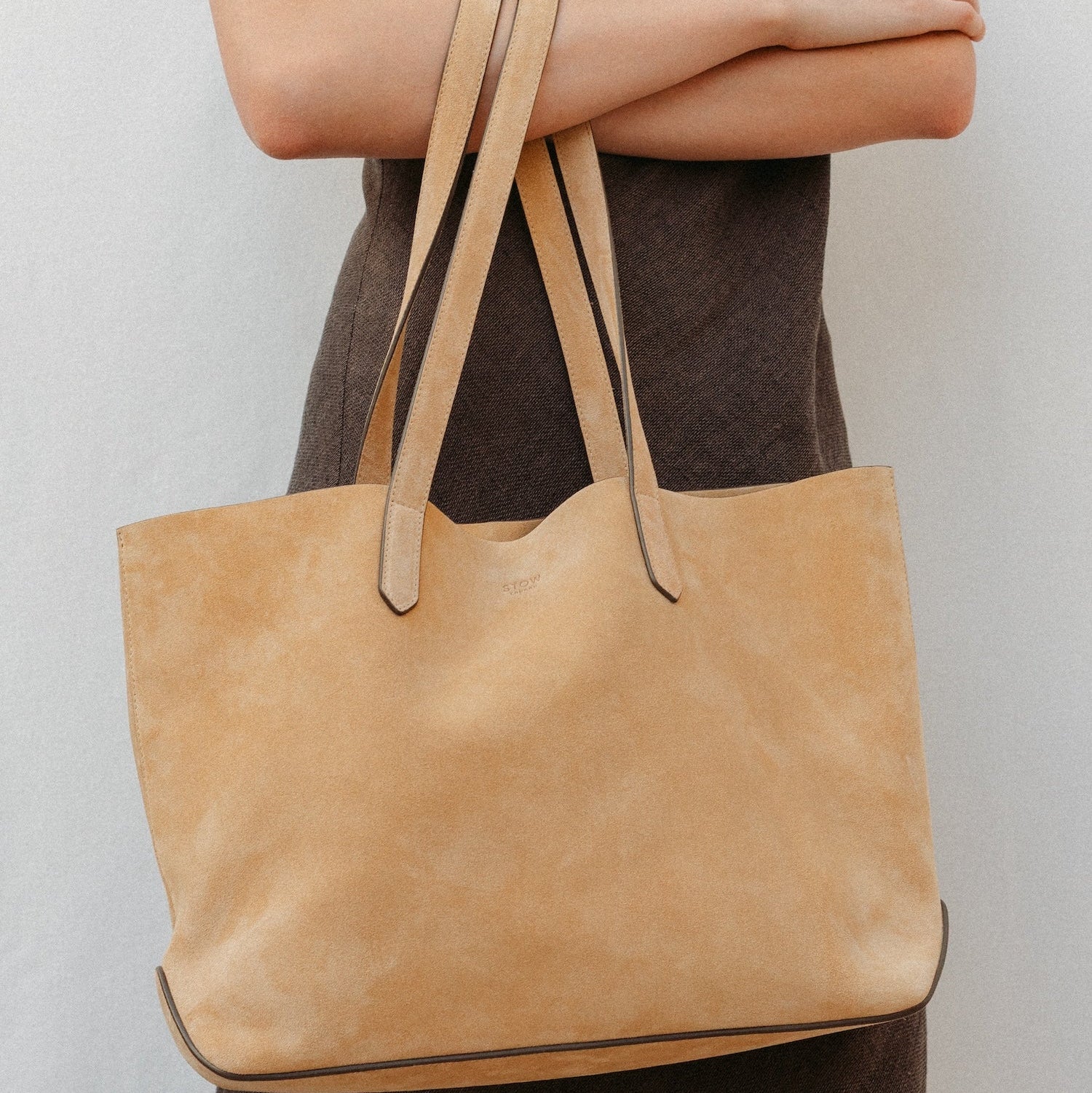 Model holding STOW London's summer Everyday Tote in Soft Sand Suede, featuring a small embossed STOW London on the front panel