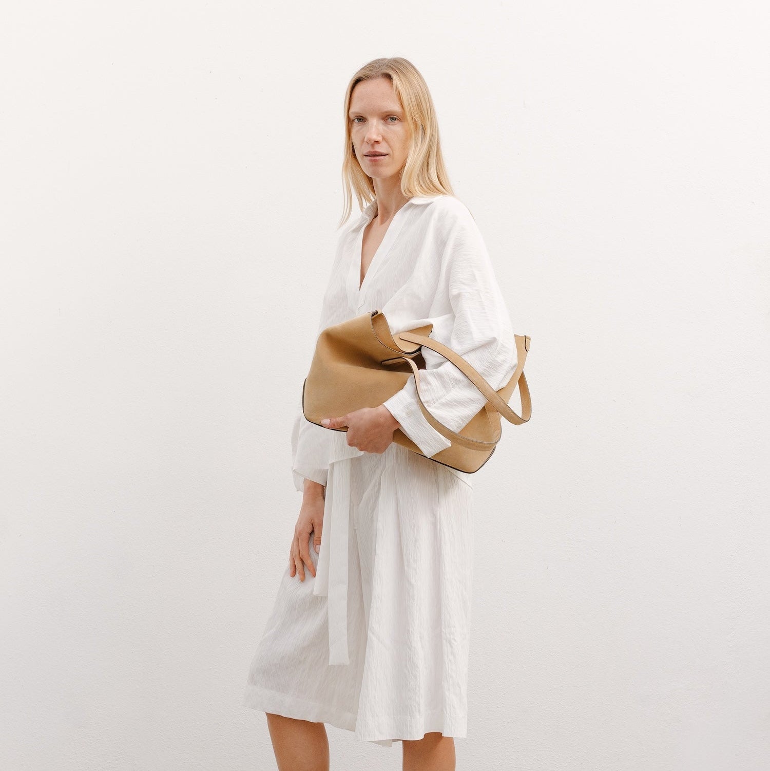 Model holding STOW London's Everyday Tote bag in Soft Sand suede featuring a small STOW London logo embossed on the front panel