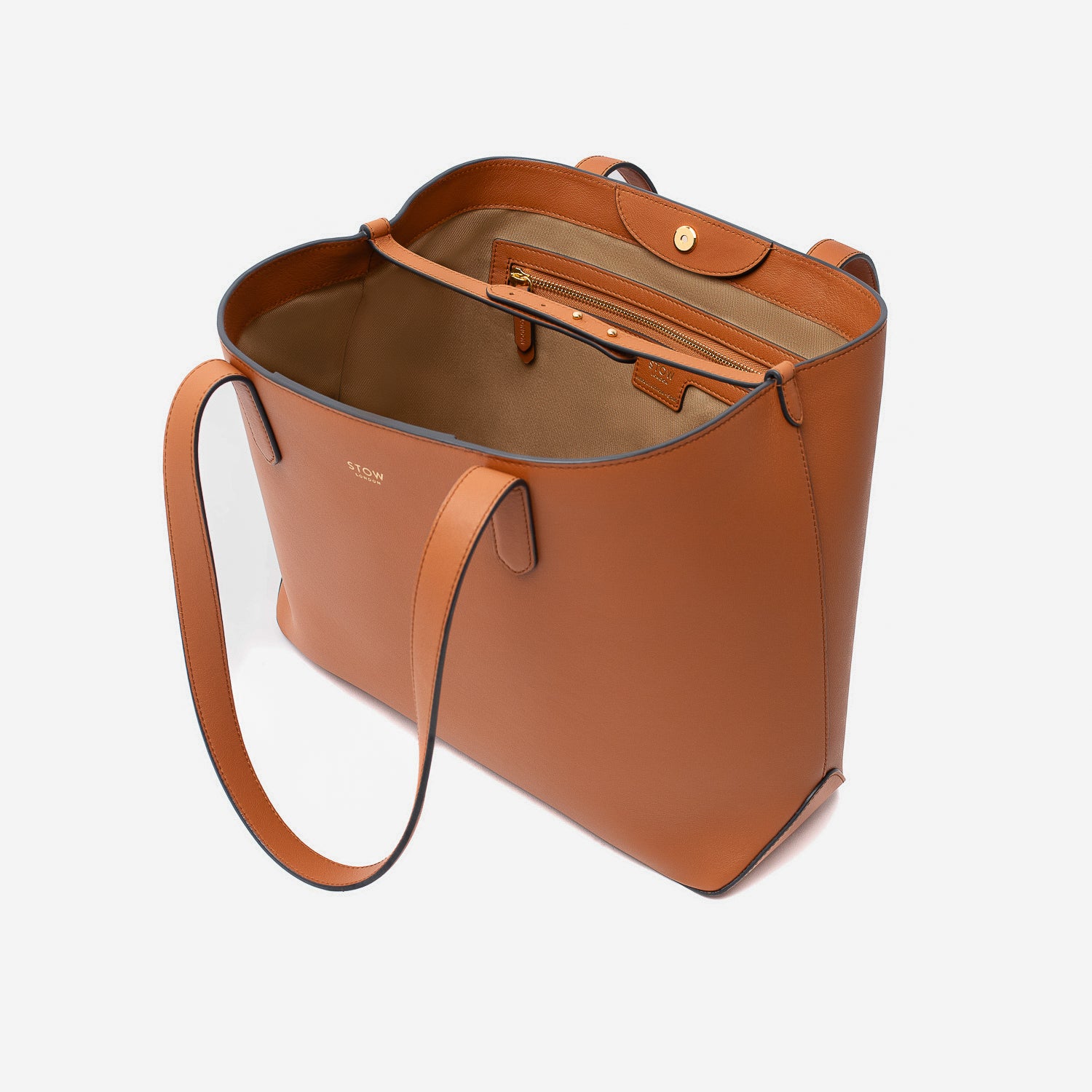 Stow London's Everyday Tote Bag in Earth Tan smooth leather with magnets open showing light beige cotton interior on a light grey background featuring the leather strap, zip pocket and magnetic closure