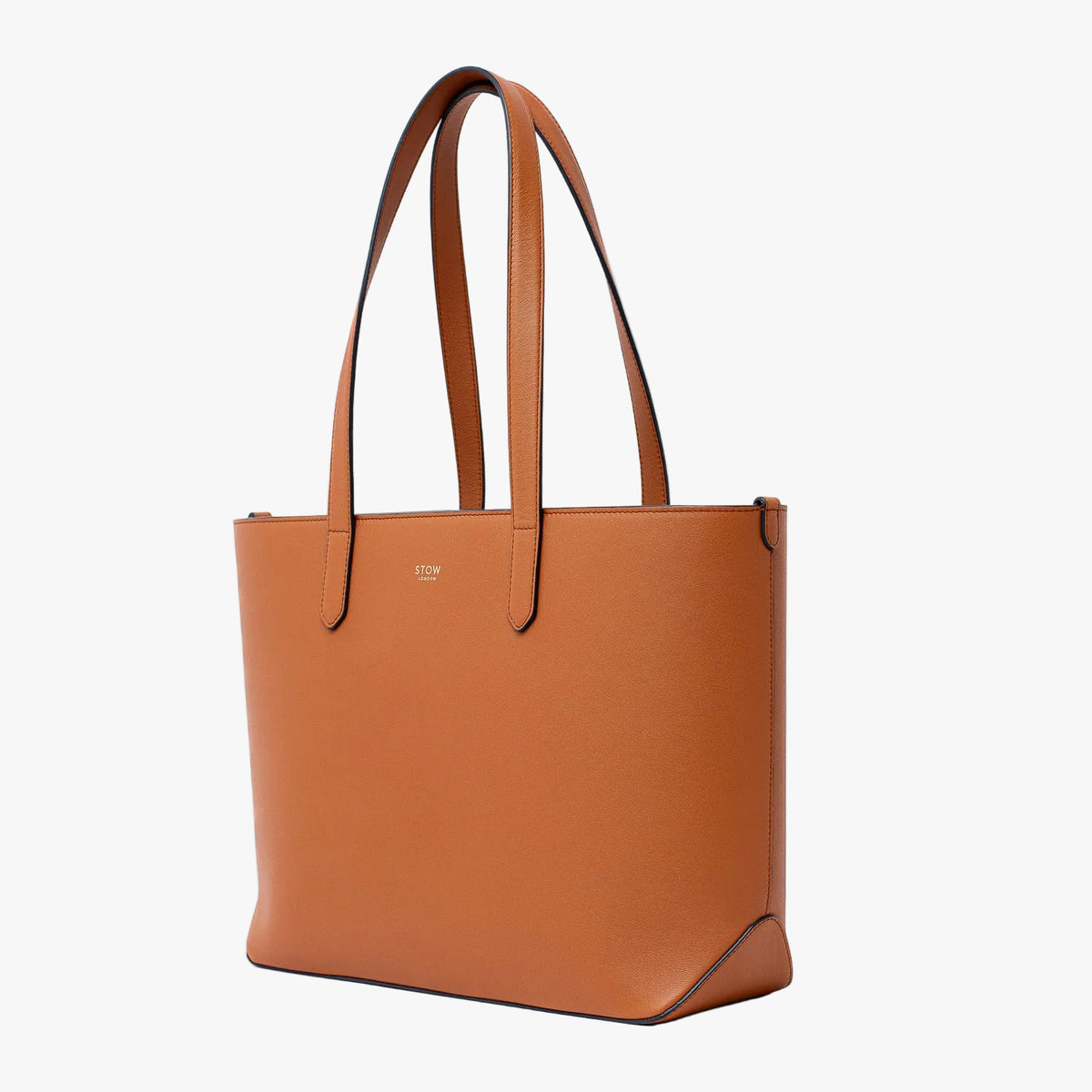 Off-axis view of Stow London's Everyday Tote Bag in Earth Tan smooth leather on a light grey background featuring gold STOW logo