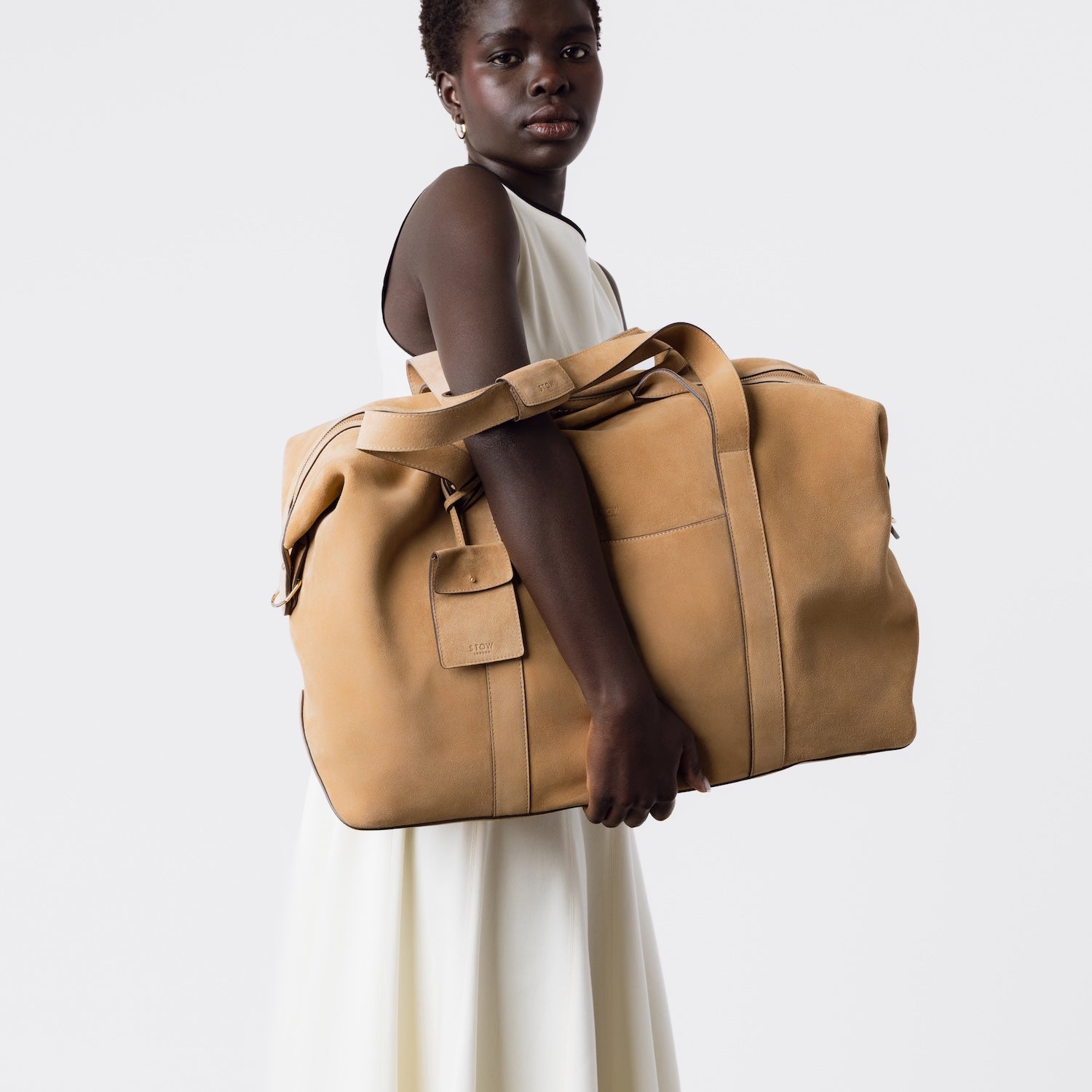 Model holding STOW London's Weekend bag in Soft Sand suede on a light grey background