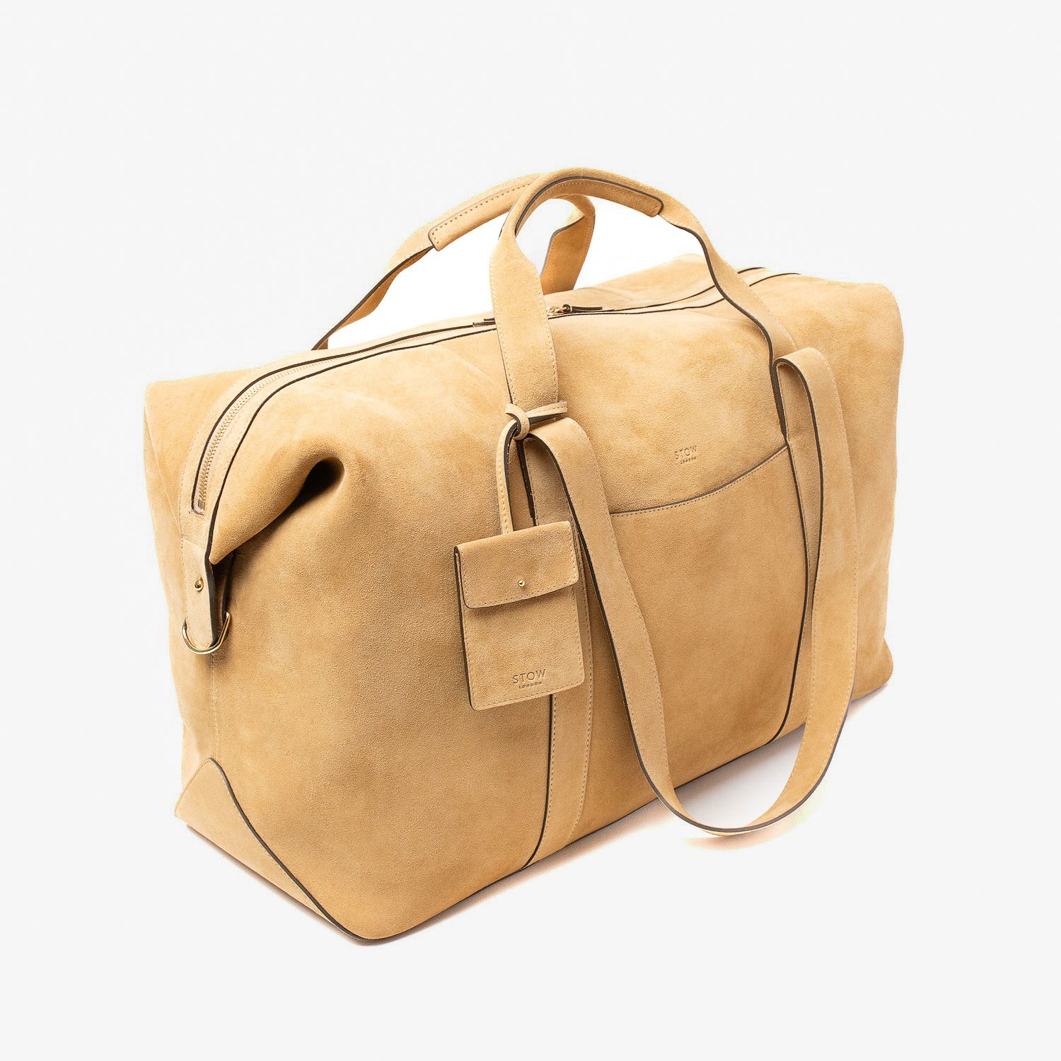 Off-axis view of STOW London's Weekend bag in Soft Sand suede leather on a light grey featuring zip closure, detachable pouch and two sets of straps on a light grey background