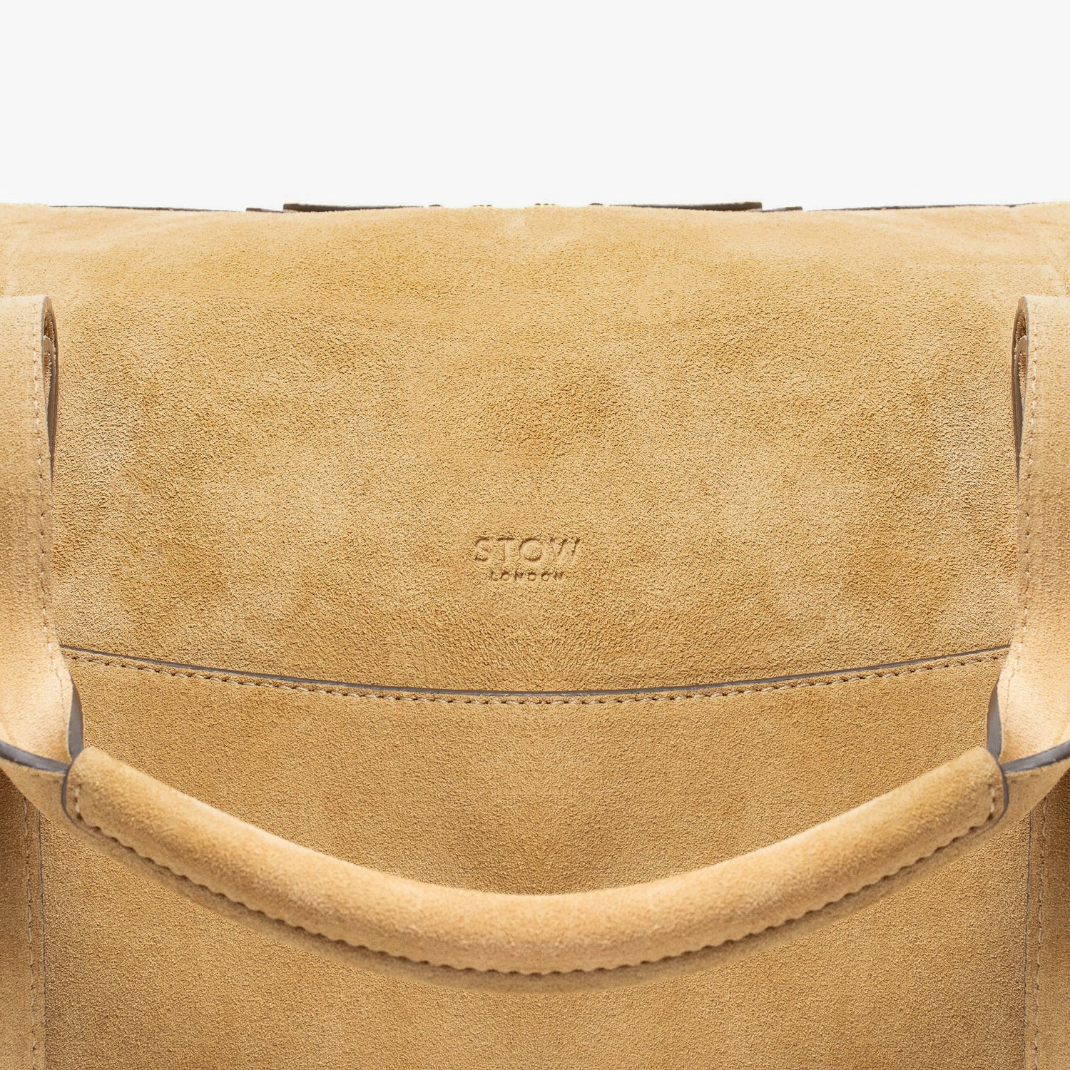 Close up of STOW London's Weekend bag in Soft Sand suede leather featuring STOW London embossed logo on a light grey background
