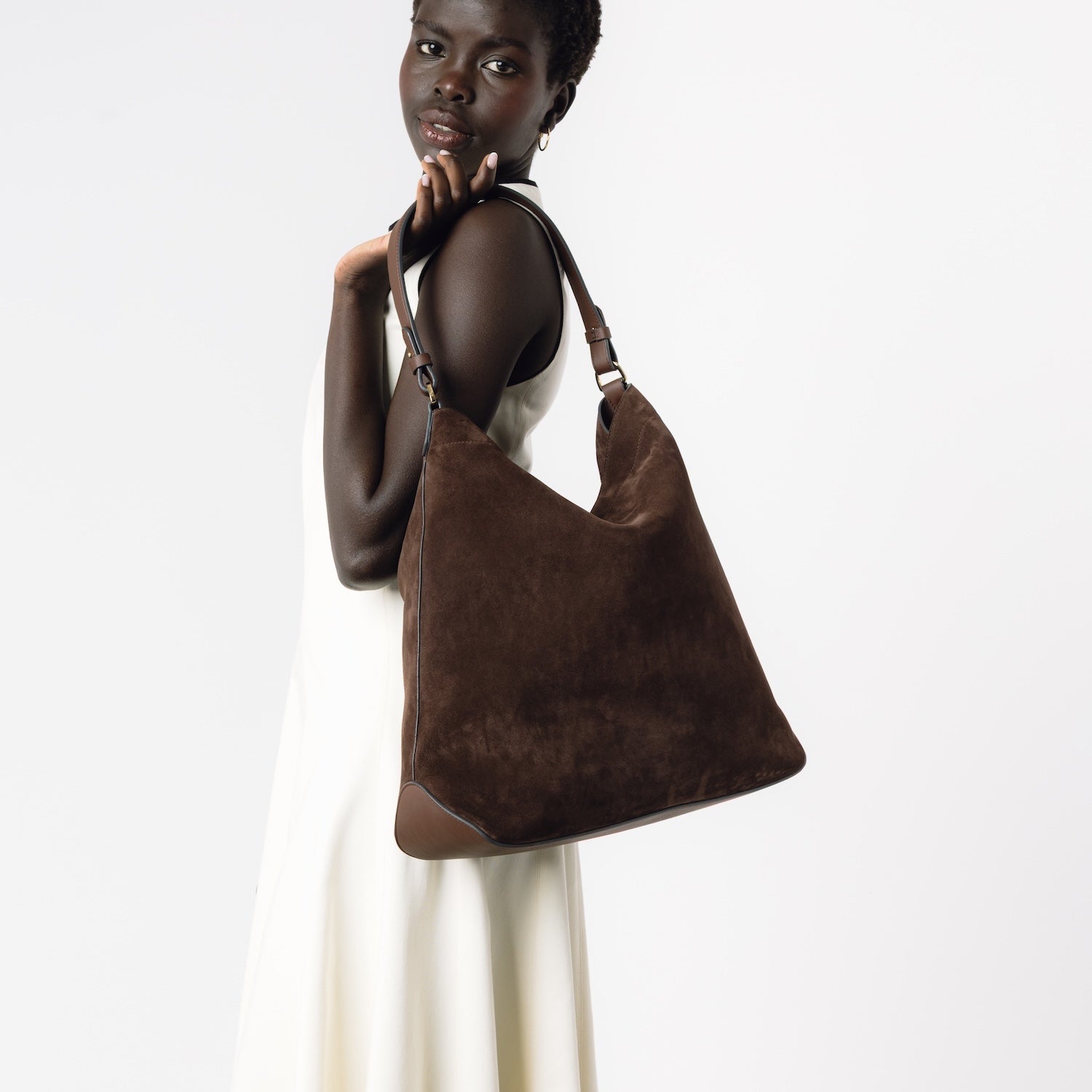 Model wearing STOW London's Maxi Curve bag in Chocolate suede leather featuring gold-coated stainless steel hardware on a light grey background