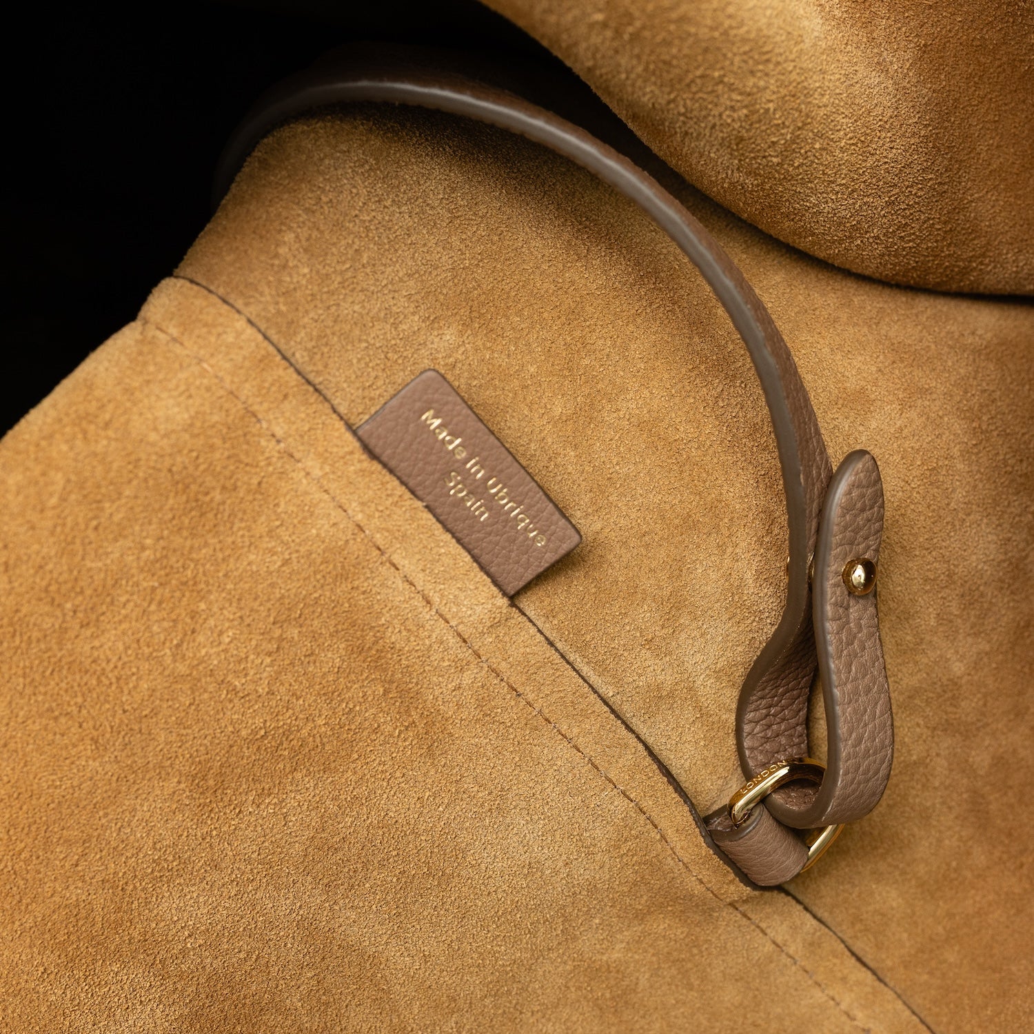 Close up of the suede interior of STOW London's Maxi Curve bag in Mocha pebbled leather featuring a gold-coated stainless steel d-ring on a light grey background