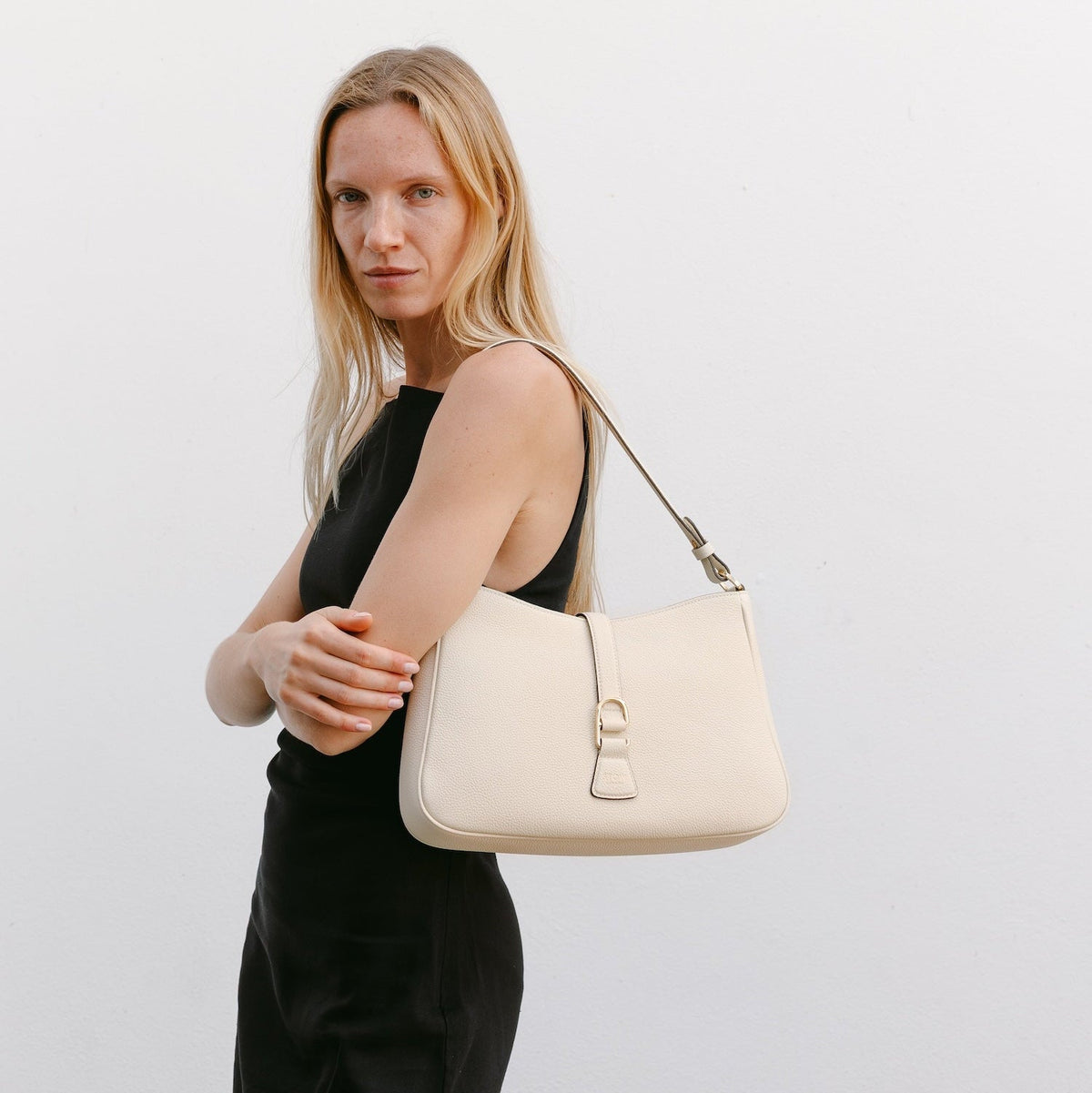 Model wearing STOW London's Beth Shoulder bag in Spring Moon pebbled leather on her shoulder featuring gold-coated stainless steel hardware and clip on a white background
