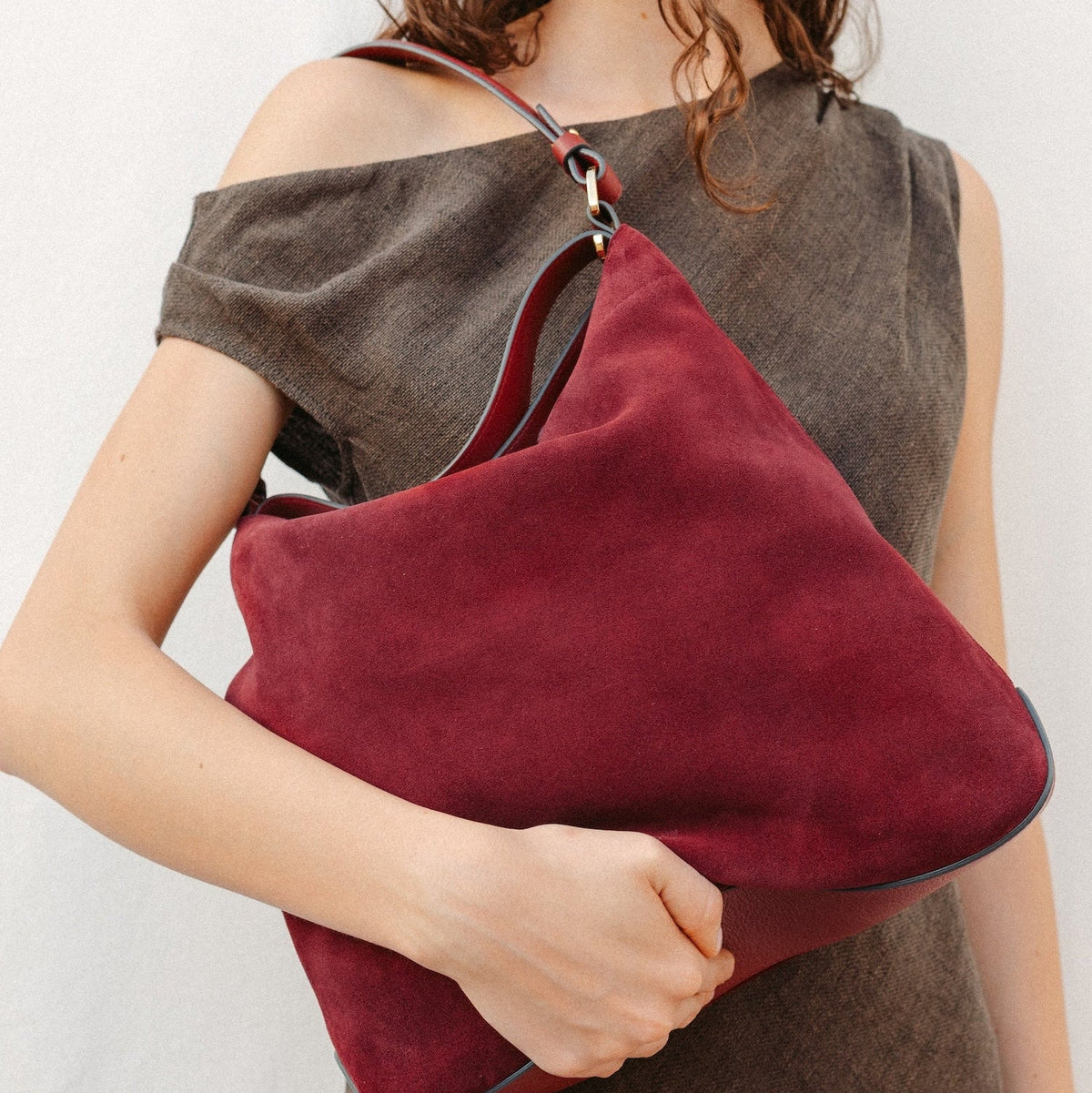 Model holding STOW London's Curve in Burgundy suede featuring the detachable shoulder strap and top handle with gold hardware