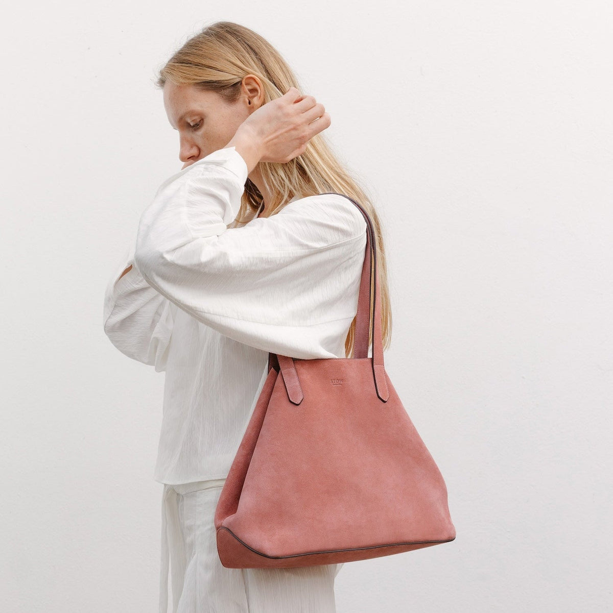 Model wearing STOW London's Everyday Tote bag in Hazy Blush suede featuring a small STOW London logo embossed on the front panel 