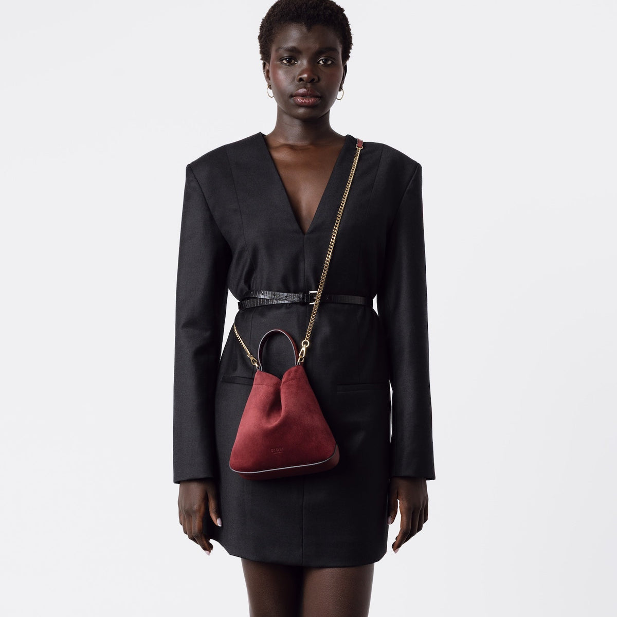 Model wearing Stow London's Mini Curve in Burgundy suede leather crossbody by gold chain strap on a white background 