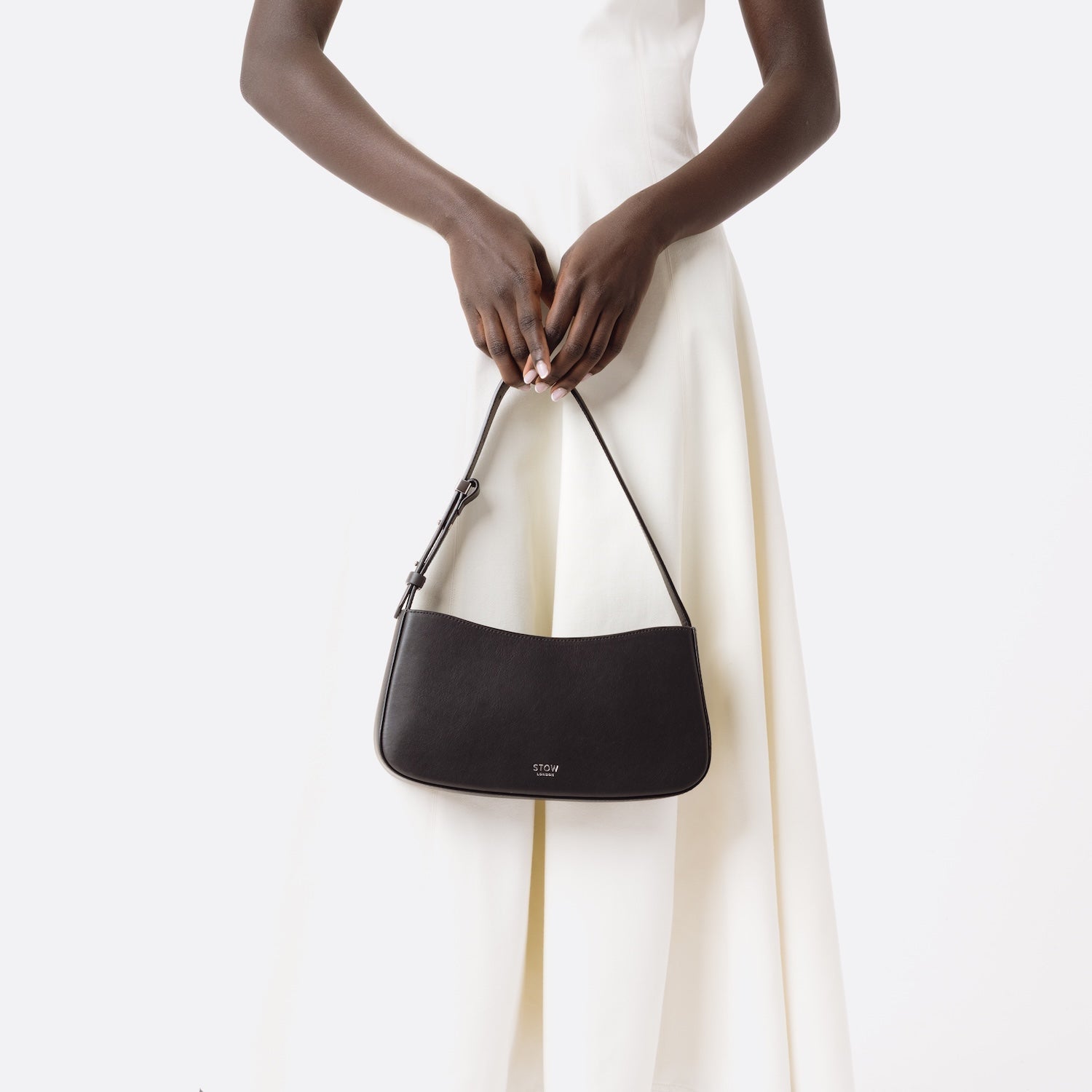 Stow London's Post Shoulder bag in Black smooth leather, held at its strap at model's front