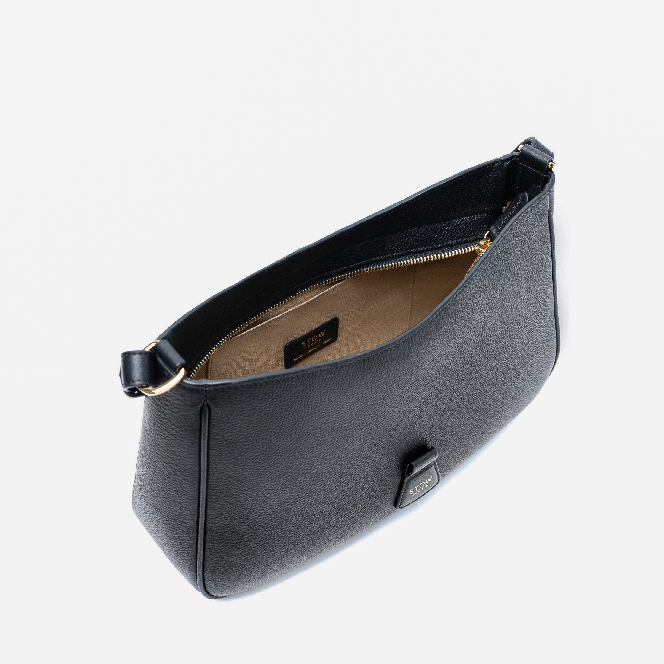 Top angled view of STOW London's Beth bag in Black pebbled and smooth leather with zipper open showing the interior cotton lining and card holder pocket, featuring gold-coated stainless steel hardware on a white background