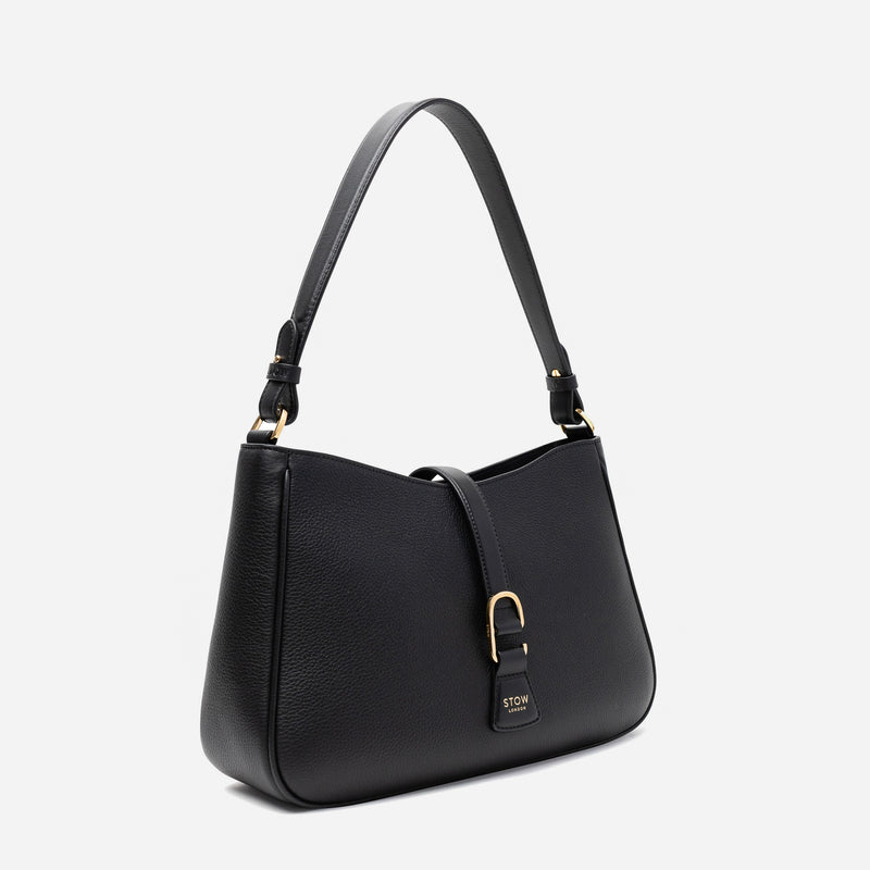 Off-axis view of STOW London's Beth bag in Black pebbled and smooth leather featuring gold-coated stainless steel hardware and clip on a white background