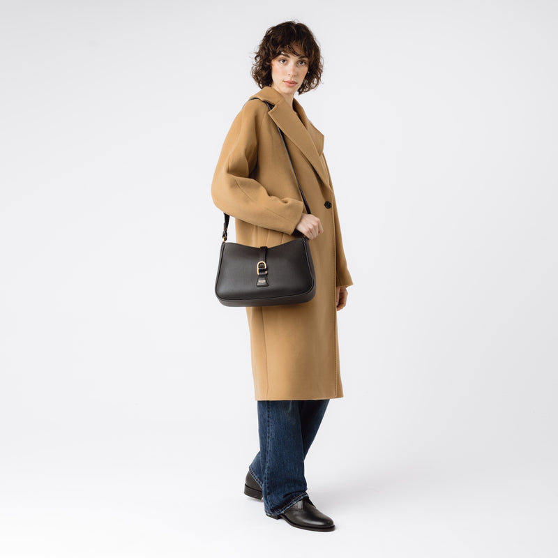 Model wearing STOW London's Beth bag and detachable crossbody strap in Black leather on her shoulder featuring gold stainless steel hardware on a white background