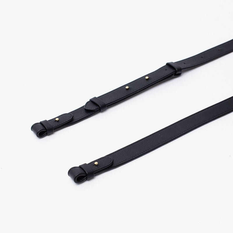 Close up shot of STOW London's detachable crossbody strap for the Beth bag in Black leather featuring gold stainless steel hardware on a white background