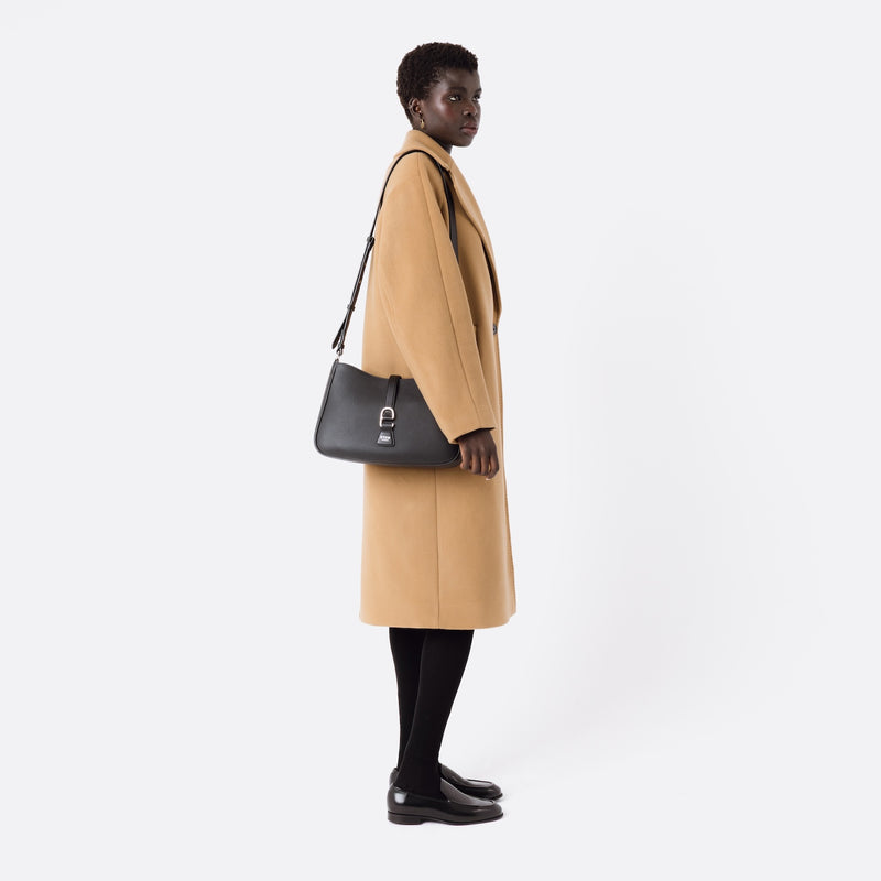 Model wearing STOW London's Beth bag with detachable crossbody strap in Black leather on her shoulder featuring silver stainless steel hardware on a white background