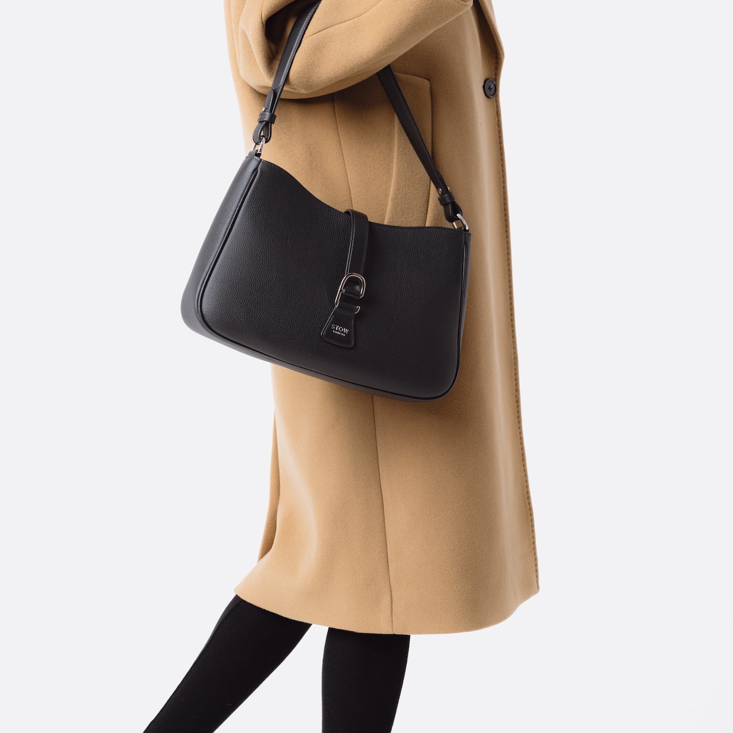 Model wearing STOW London's Beth bag in Black pebbled and smooth leather on her arm featuring silver stainless steel hardware and clip on a white background