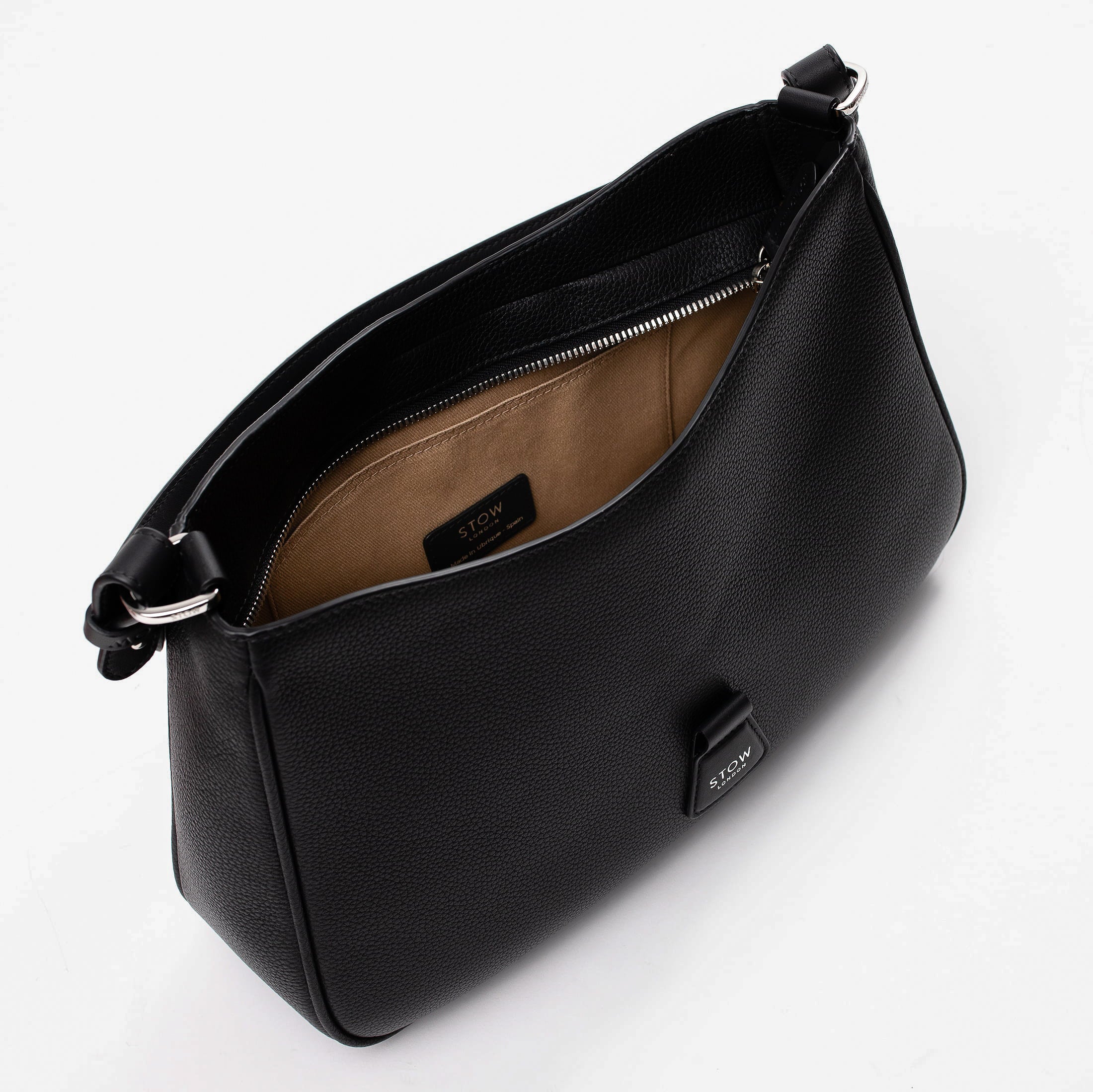 Top angled view of STOW London's Beth bag in Black pebbled and smooth leather with zipper open showing the interior cotton lining and card holder pocket, featuring silver stainless steel hardware on a white background