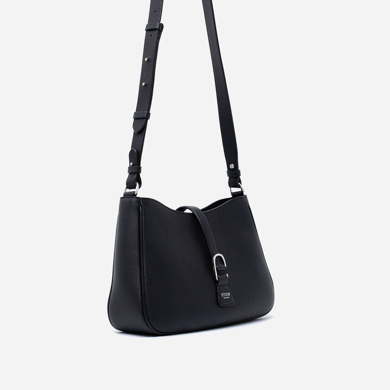 Off-axis view of STOW London's Beth bag and detachable crossbody strap in Black leather featuring silver stainless steel hardware on a white background
