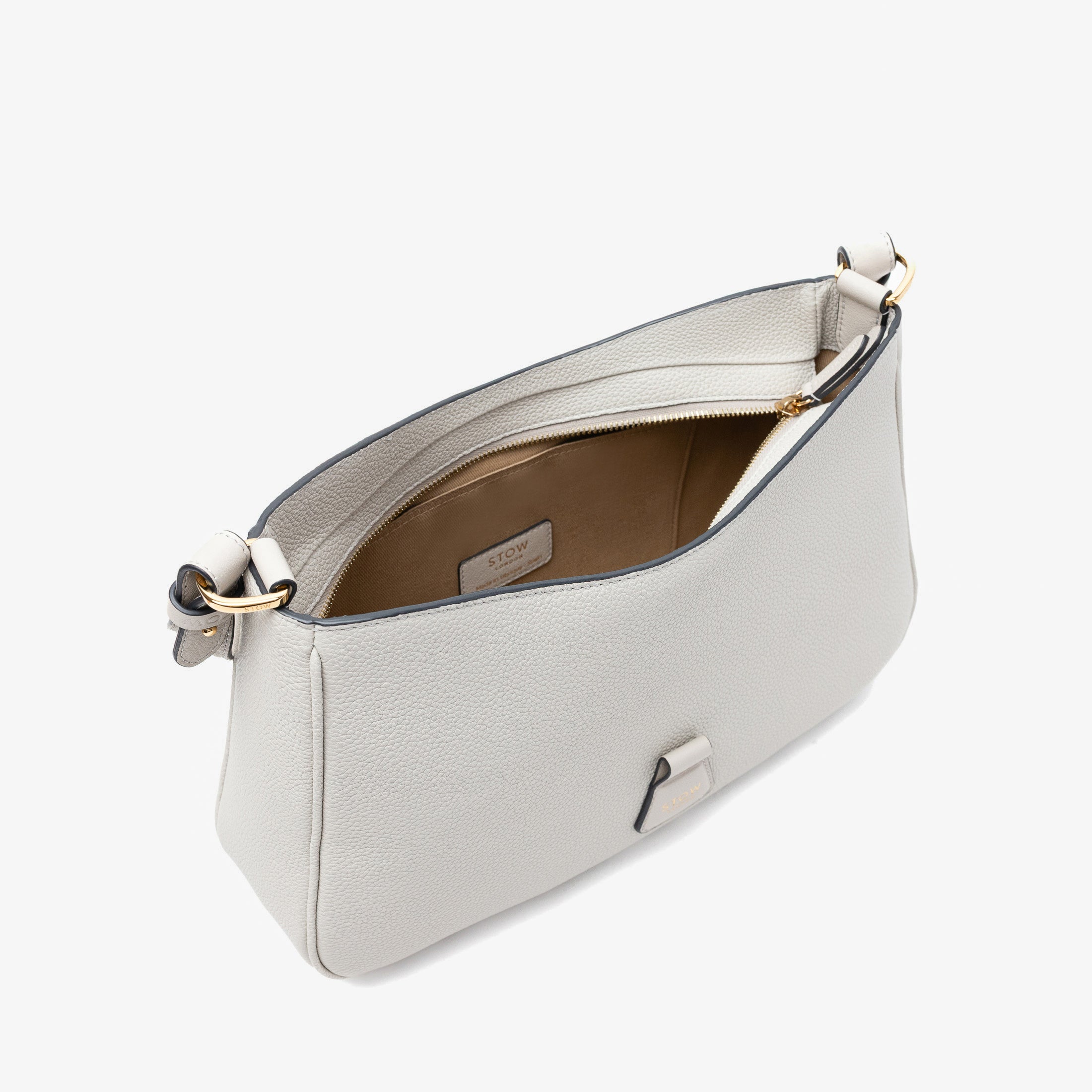 Top angled view of STOW London's Beth bag in Cloud Grey pebbled and smooth leather with zipper open showing the interior cotton lining and card holder pocket, featuring gold-coated stainless steel hardware on a white background