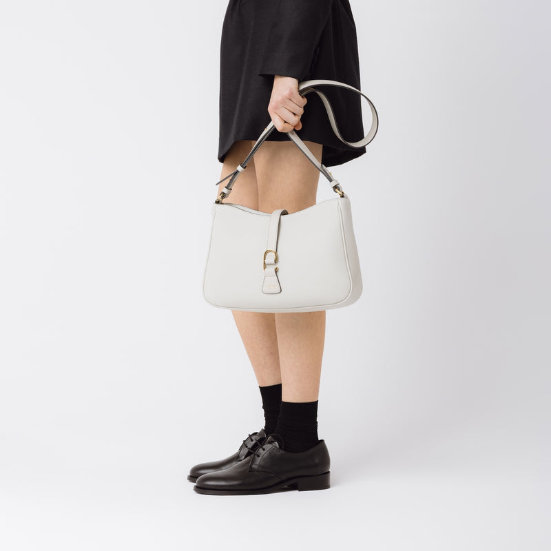 Model holding STOW London's Beth bag and detachable crossbody strap in Cloud Grey leather featuring gold stainless steel hardware on a white background
